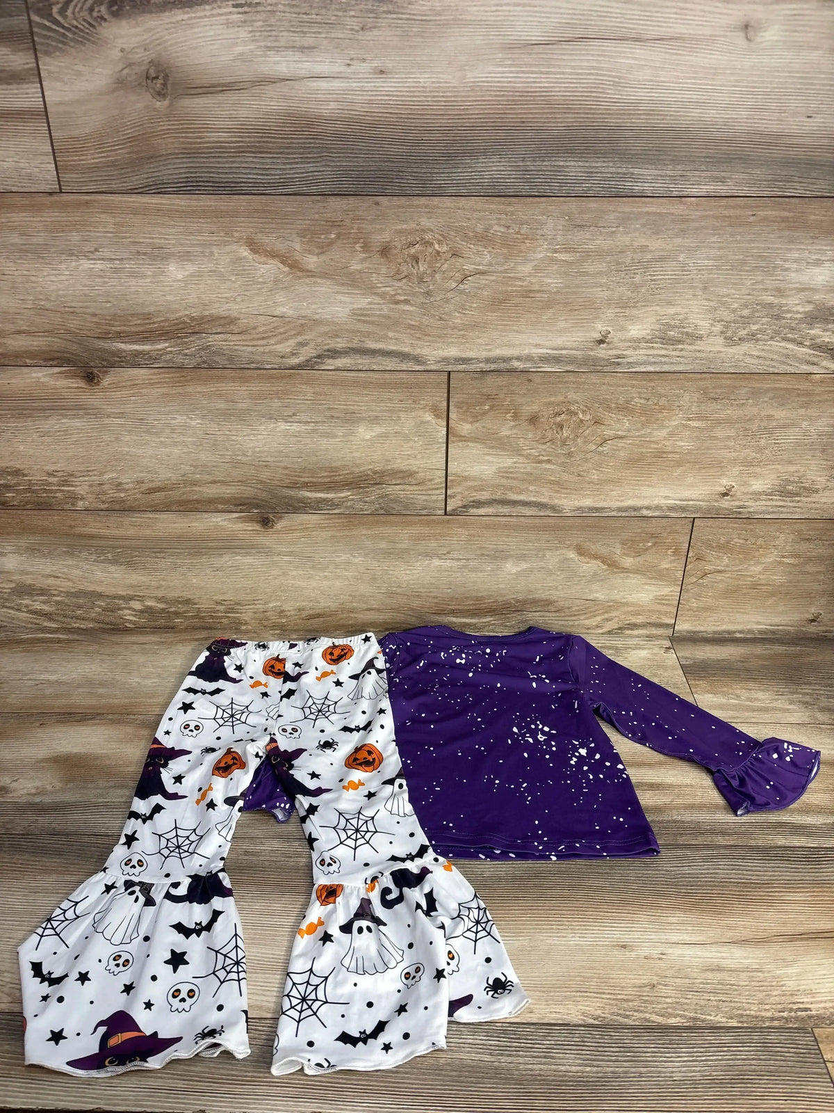 Kids Halloween outfit with purple splatter top and witch-themed print pants on wood floor