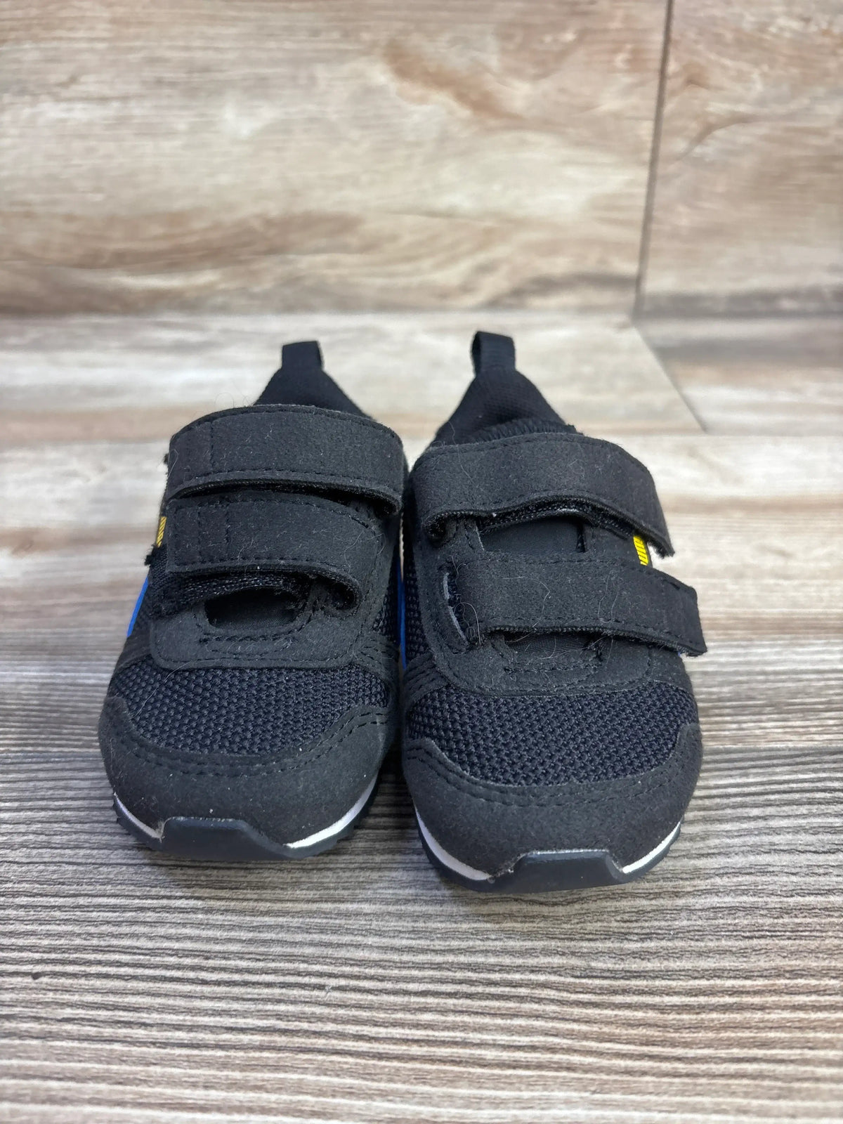 Front view of black Puma R78 double strap sneakers showcasing two hook-and-loop straps and cushioned soles on a wood-look surface