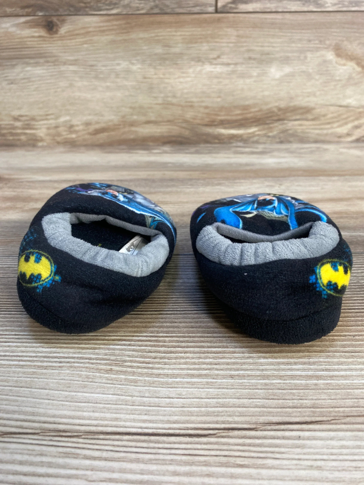 Black baby slippers with Batman logos on wooden floor