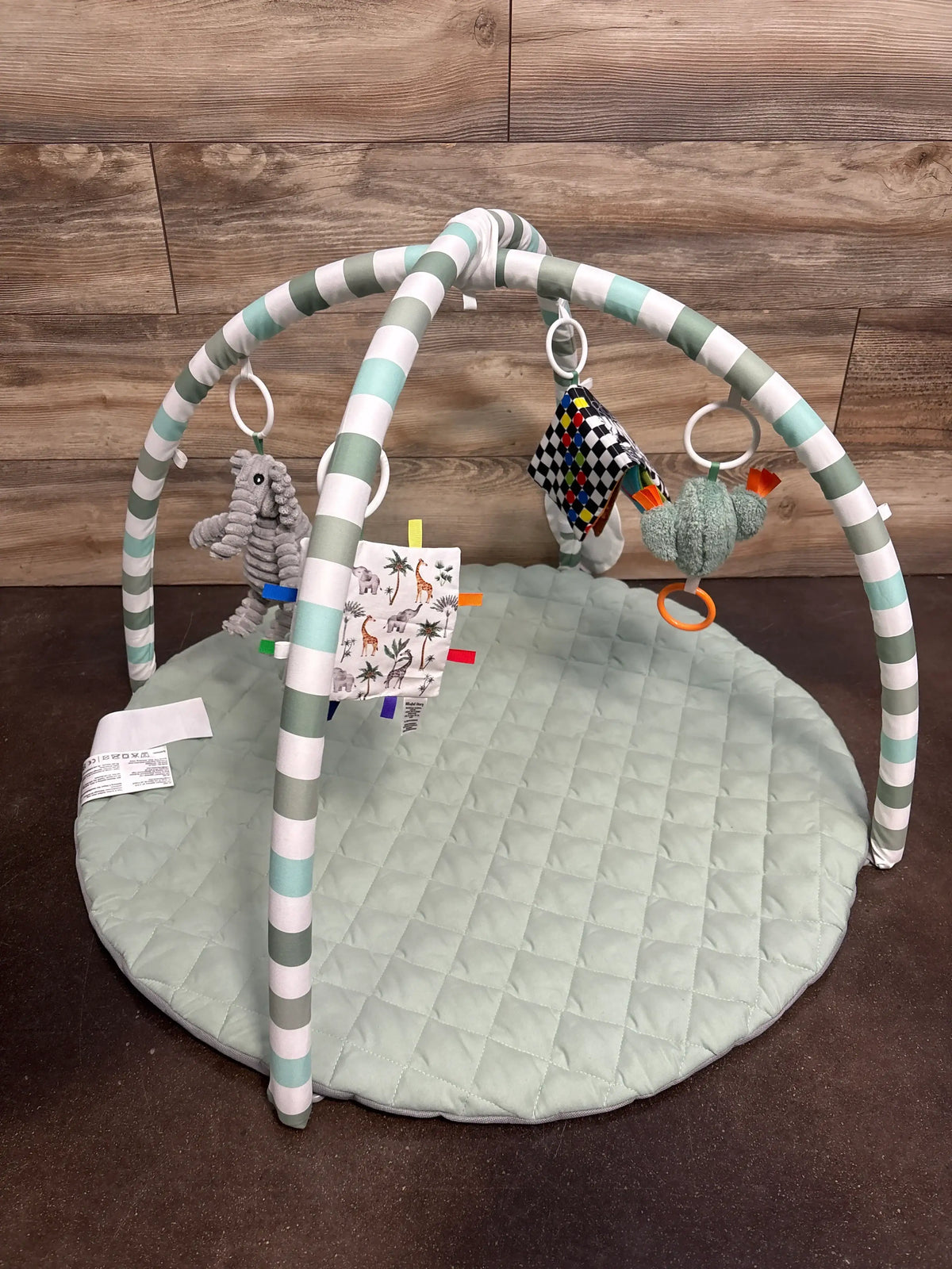 Angled view of sage green baby play gym activity mat showcasing striped arches and hanging sensory toys