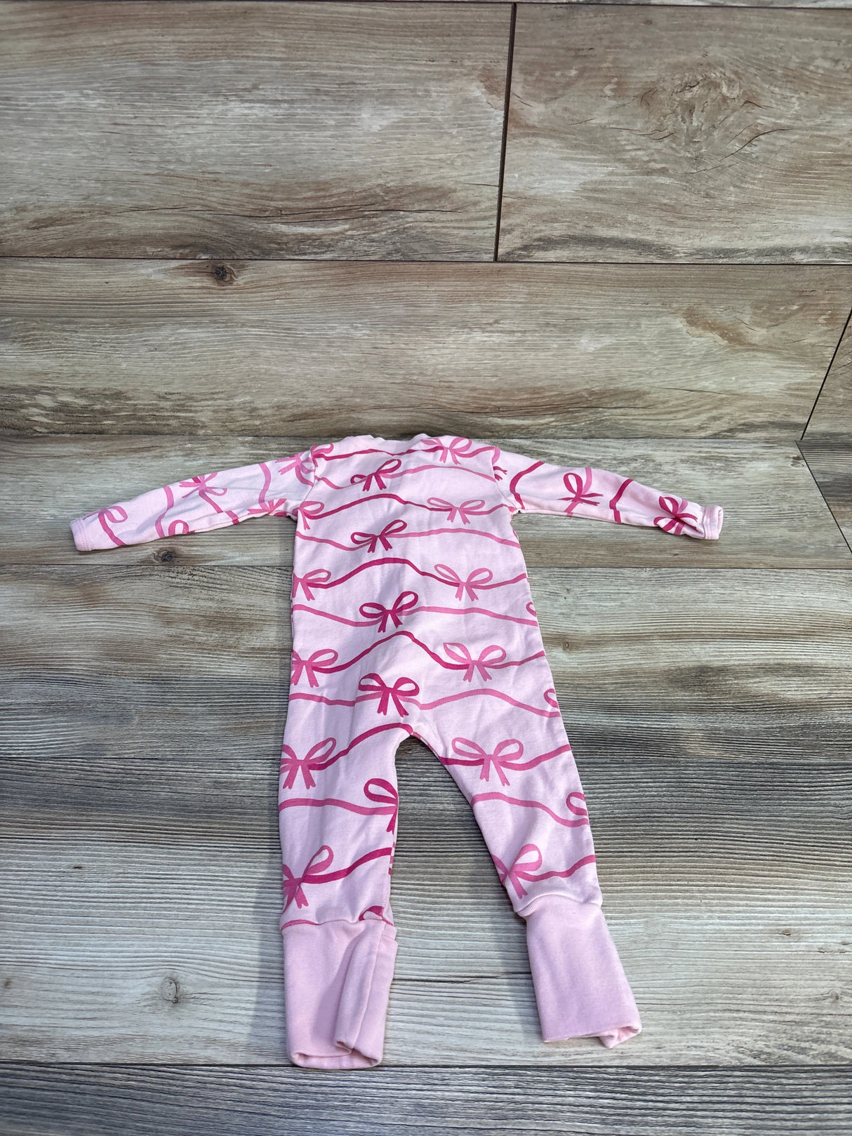 Flat lay of Paris Hilton x Monica + Andy pink baby sleeper with pink bow print and fold-over ankle cuffs on wood