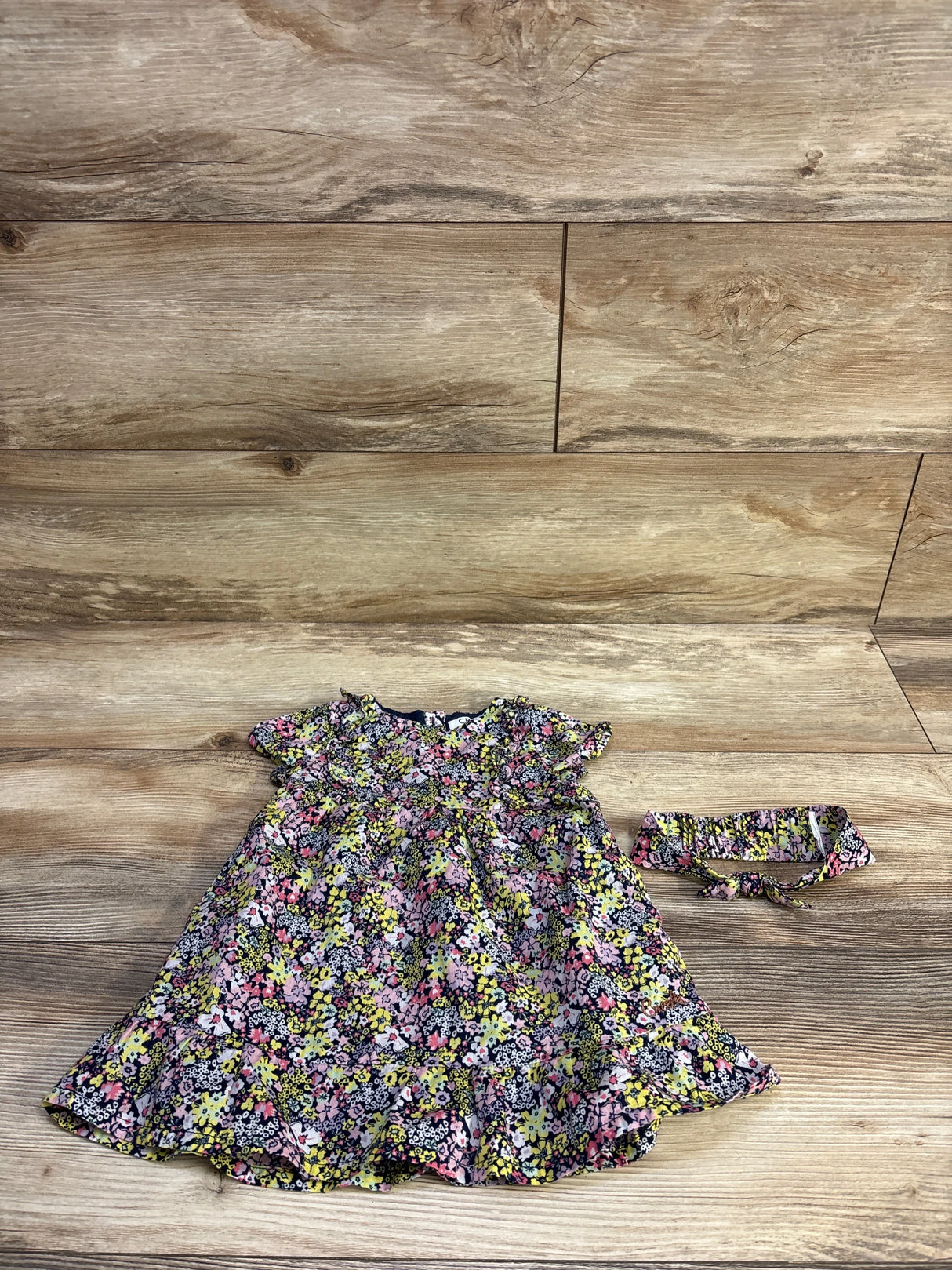 Flat lay of navy floral baby dress with matching headband showing short flutter sleeves and ruffled hem on wood background