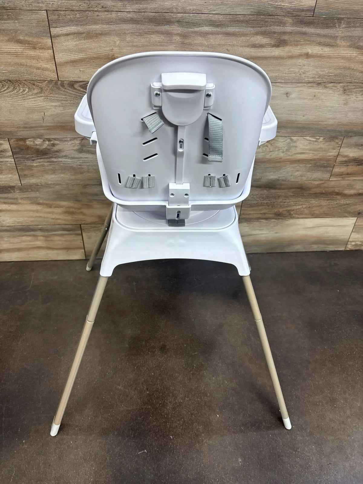Rear view of Safety 1st Grow and Go Rotating High Chair in French Gray showcasing safety straps on a wood floor