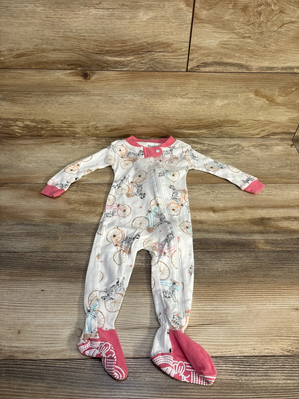 Front view of Burt’s Bees Baby organic sleeper in white, showcasing bicycle print, zipper, and pink foot cuffs on a wood floor