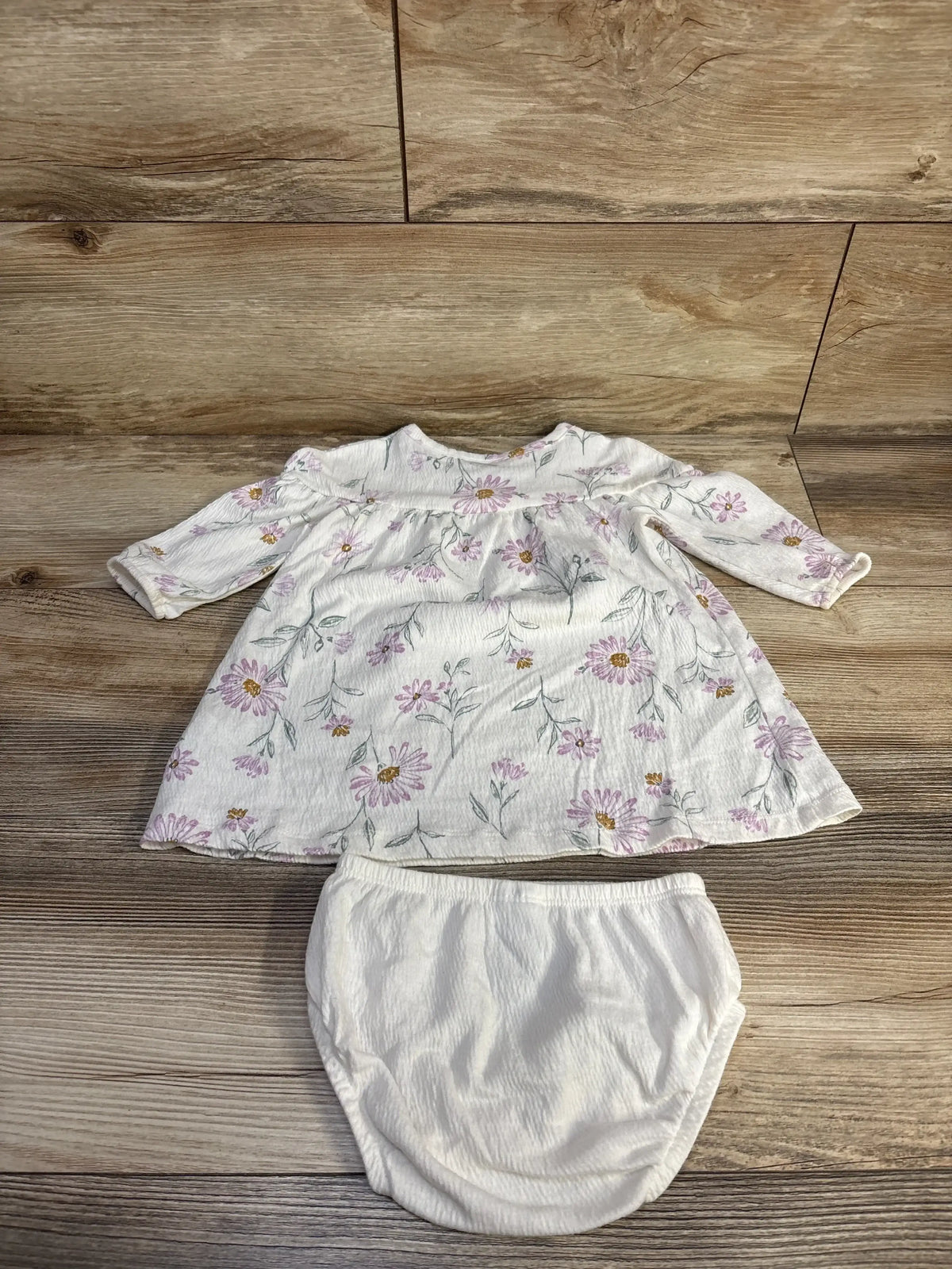 Top-down view of Carter's 2-piece white henley dress with pink floral print and matching white bloomers on wood background