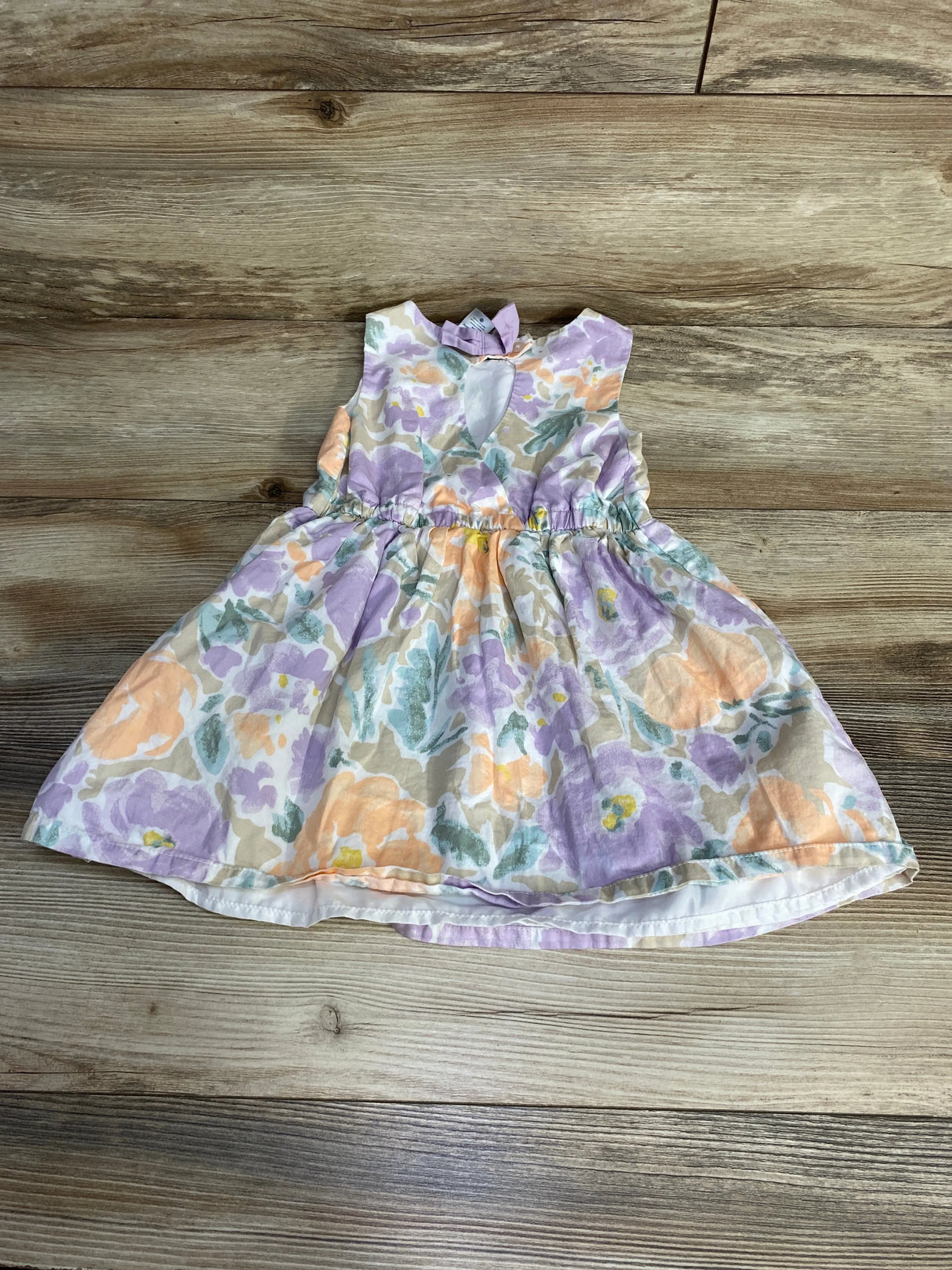 Flat lay of toddler floral dress with pastel purple and peach flowers, keyhole back and gathered waist on wood background