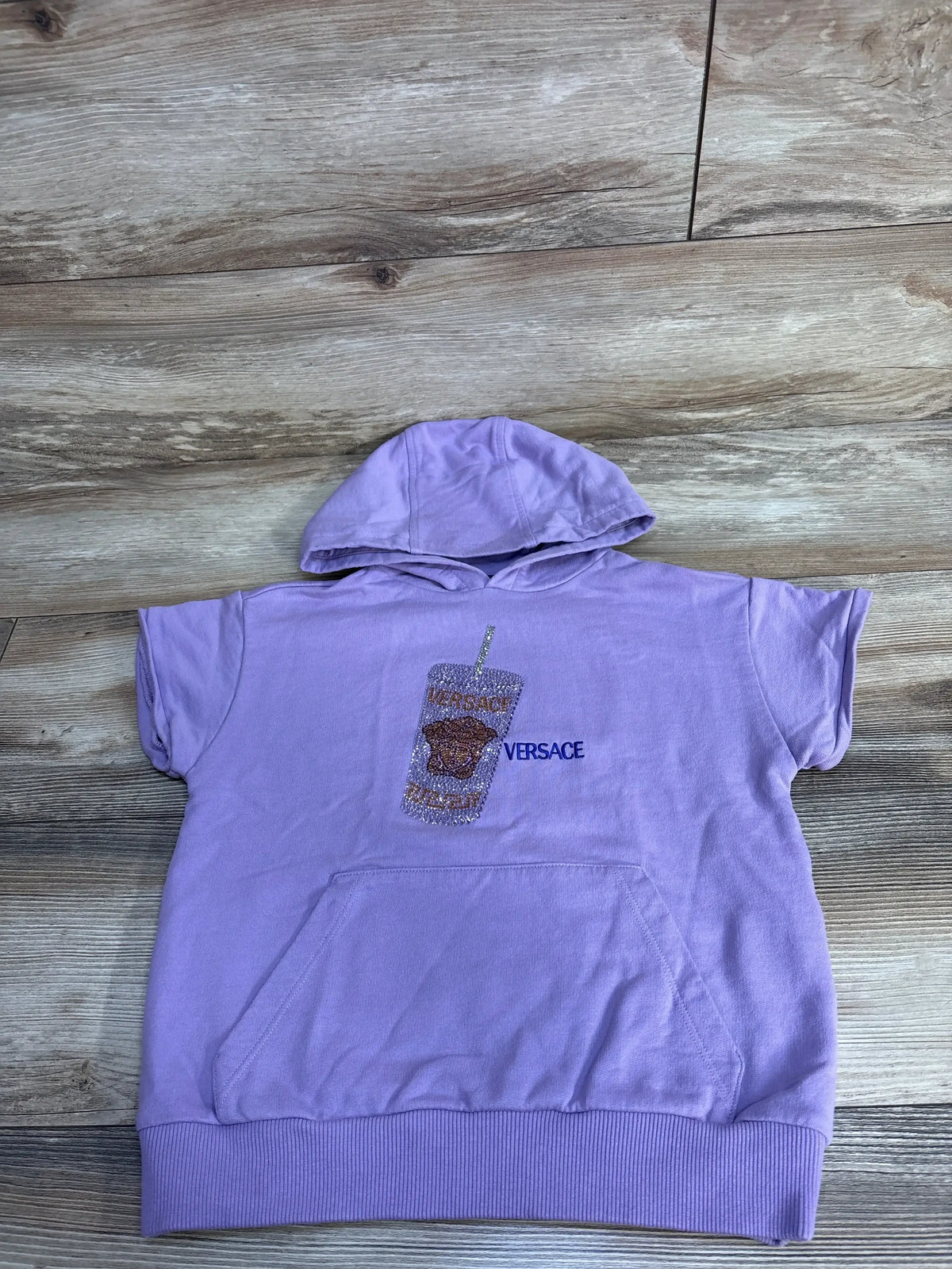 Lilac short-sleeve Versace hoodie with glitter drink graphic, wood background