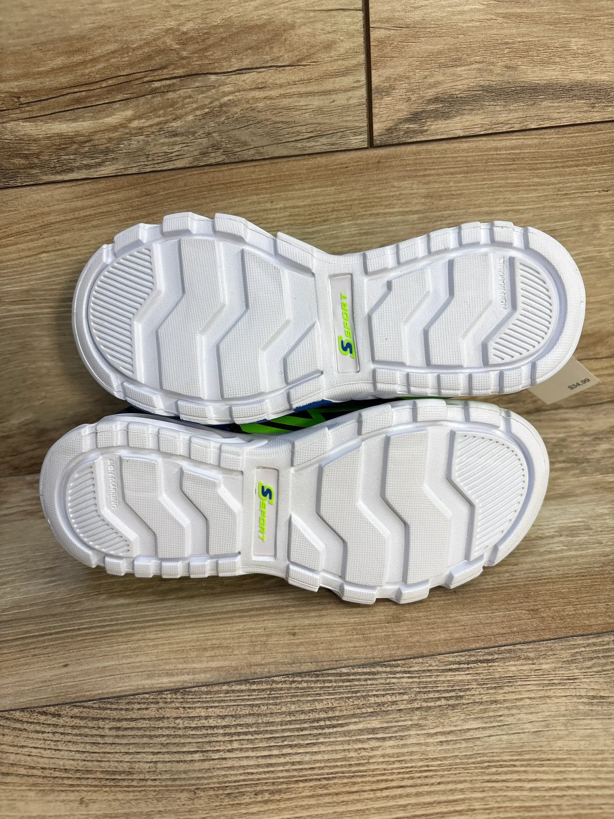 Sole view of Skechers Lights Ottis sneaker size 3Y showing white treaded outsole with green S logo on wood floor