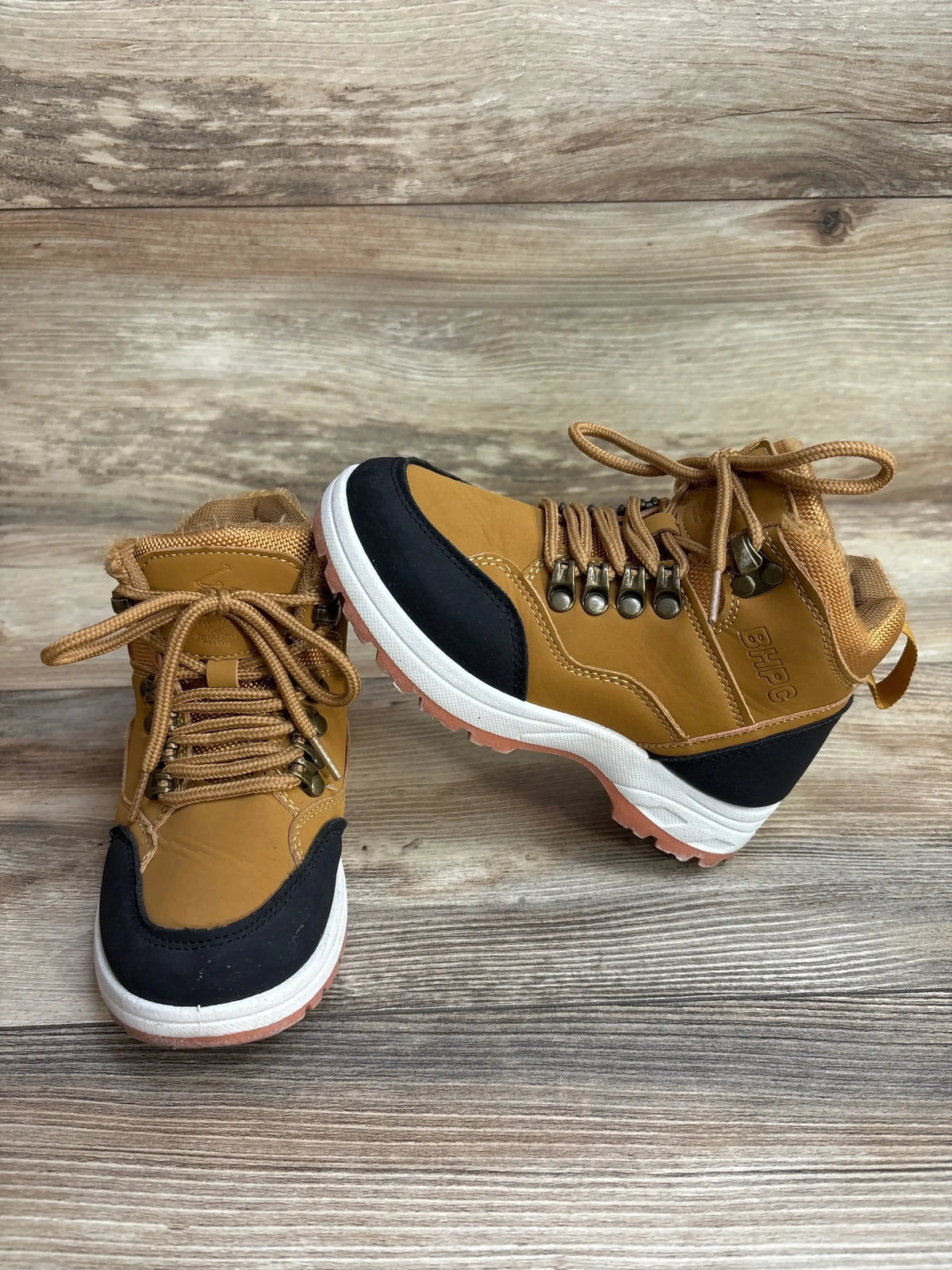 Brown and black kids hiking boots with laces on wood background