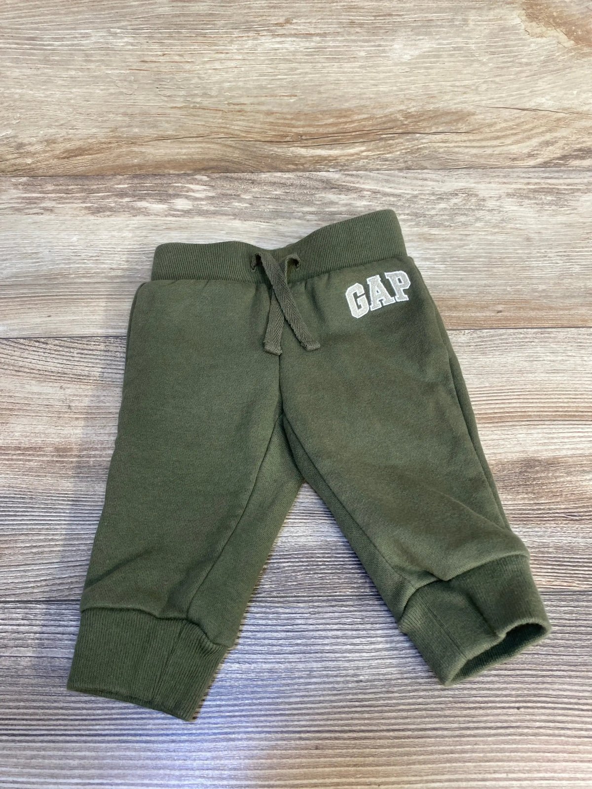 Olive green baby jogger pants with GAP logo, kids clothing on wood background