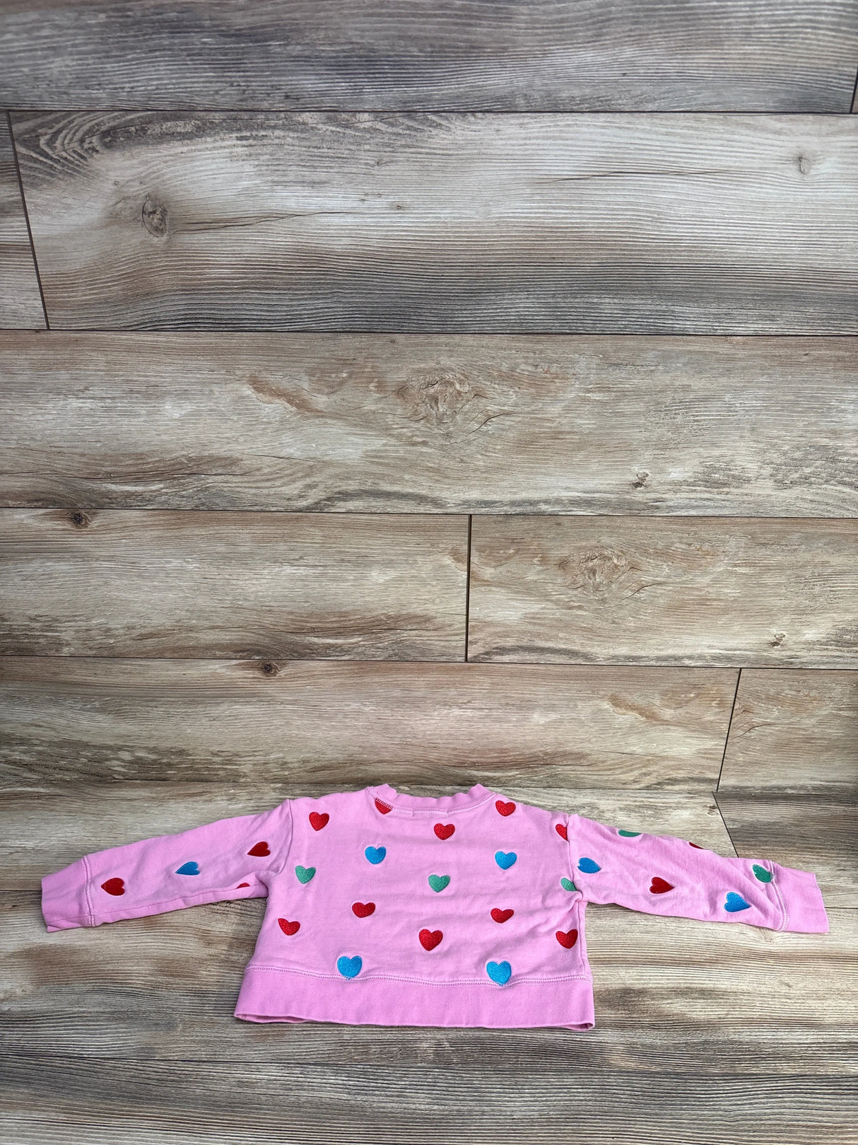 Flat lay of Stella McCartney pink pullover sweatshirt 4T showing red, blue and green heart appliques on wood floor