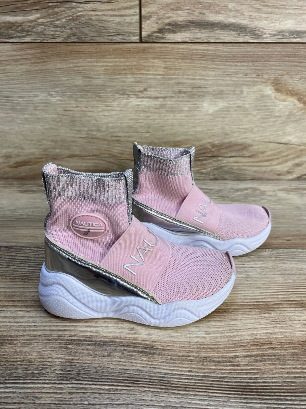 Three-quarter view of Nautica slip-on sock style sneakers sz 6c showcasing pink knit uppers with silver accents and chunky white sole on wood