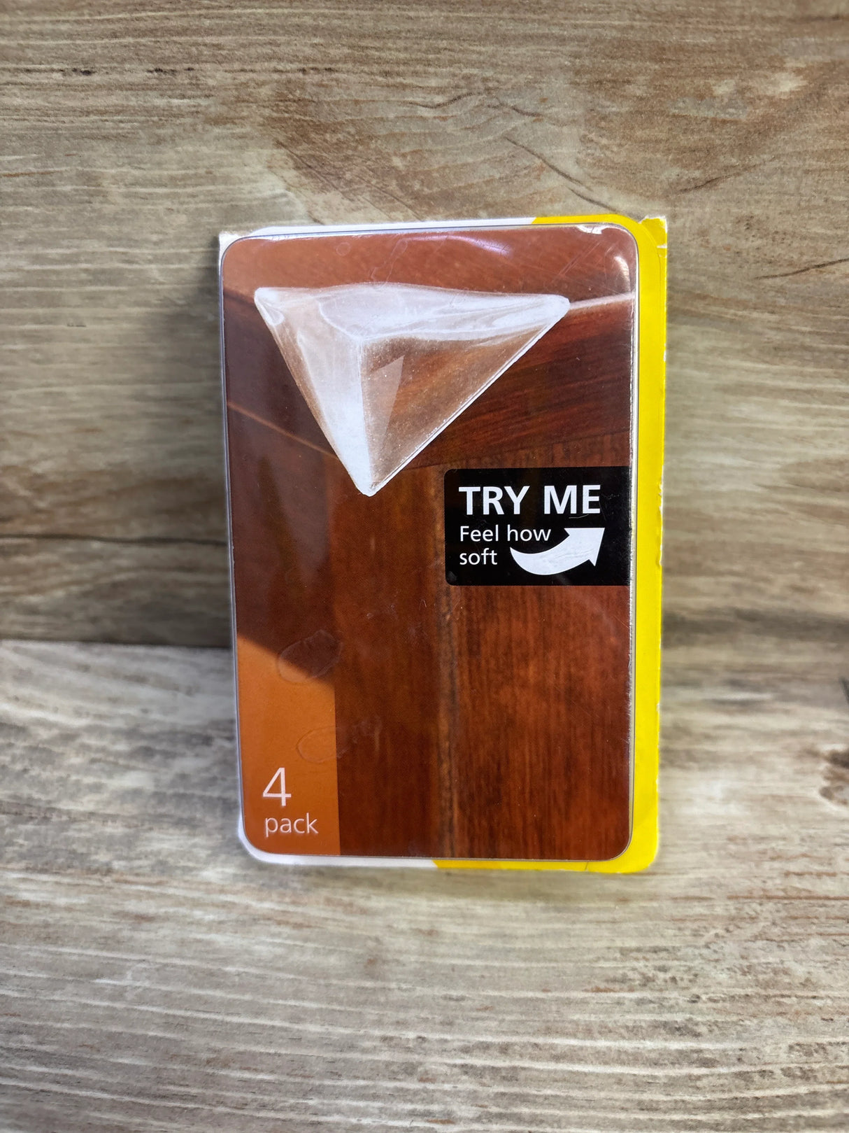 Front view of Safety 1st Clearly Soft corner guard showing clear triangular sample and TRY ME label on wood background