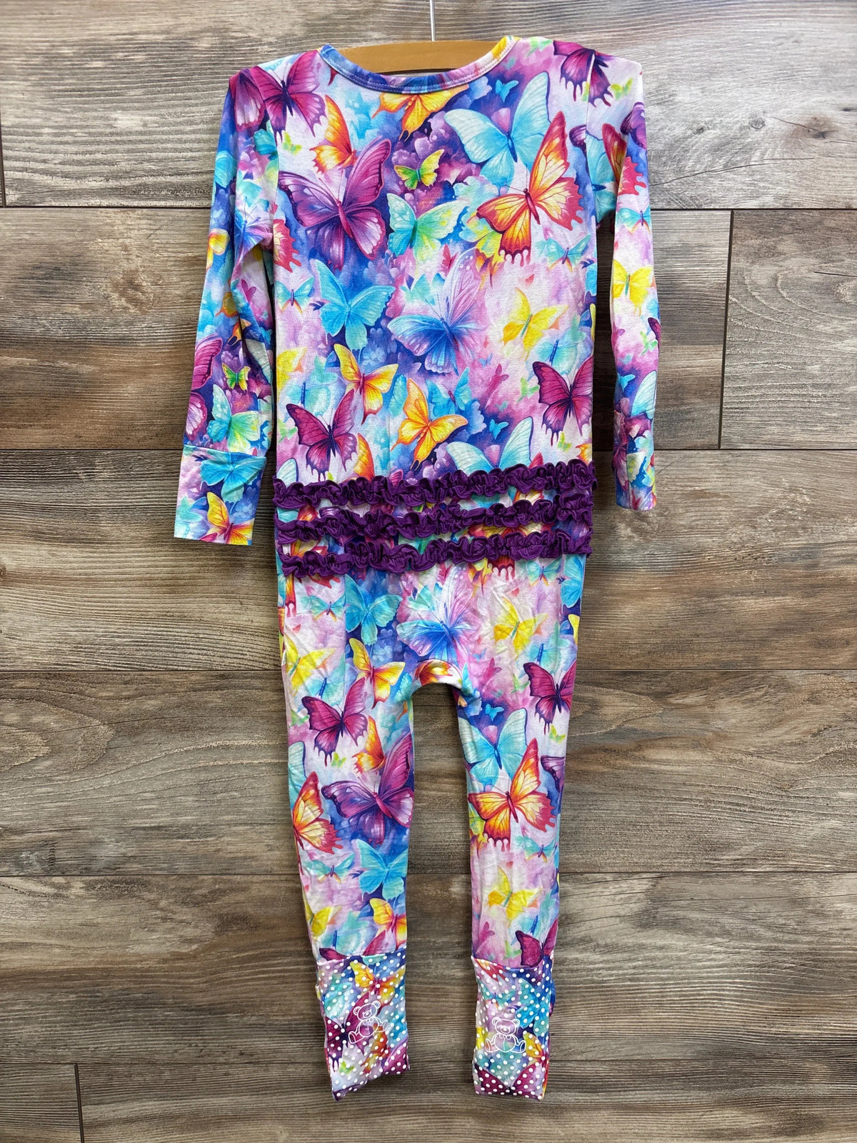 Front view of bamboo butterfly convertible footie with colorful butterfly print and purple ruffle trim on wood background