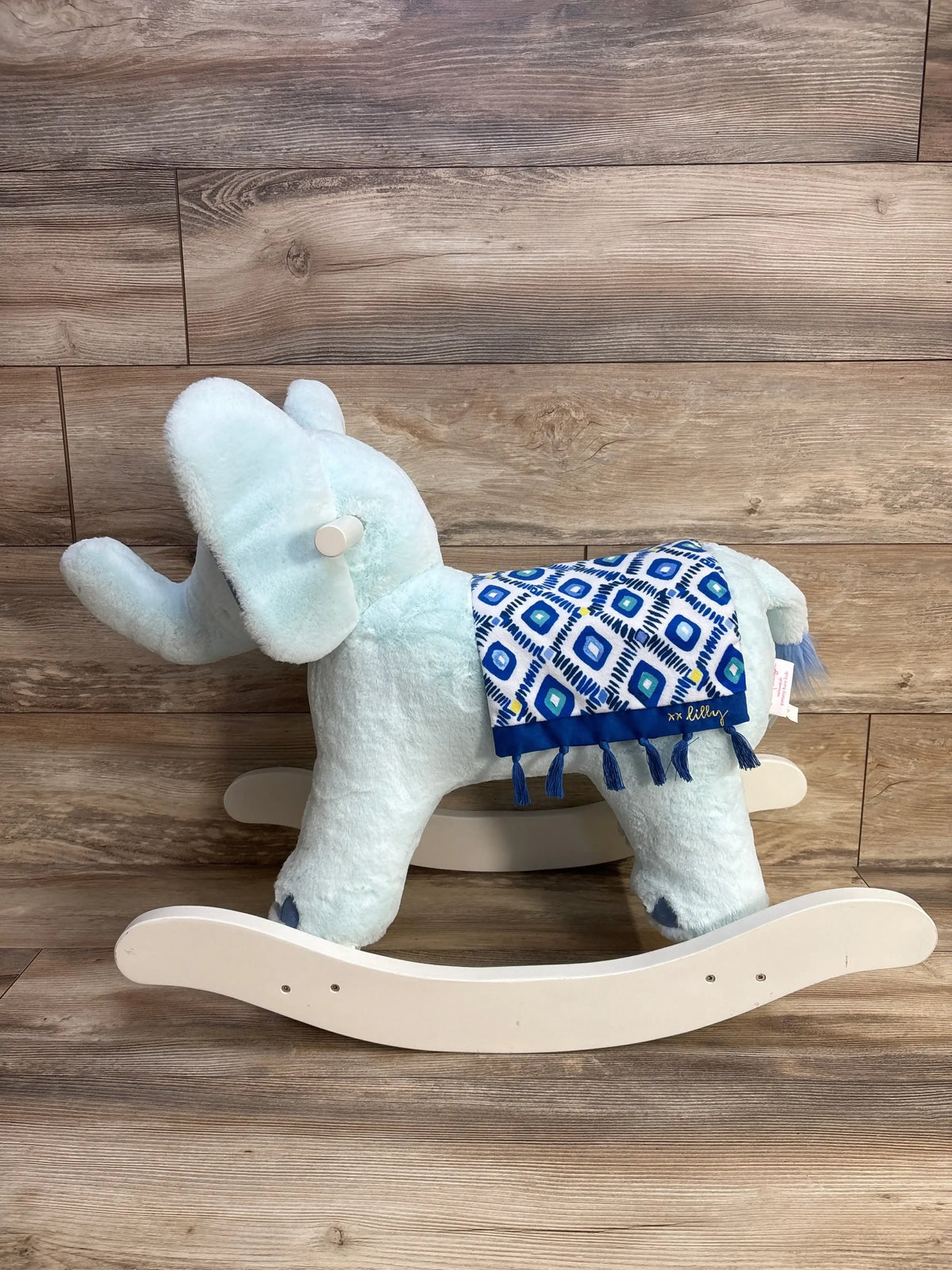 Side view of Lilly Pulitzer elephant rocker with light blue plush body, patterned blue saddle with tassels and wooden rockers