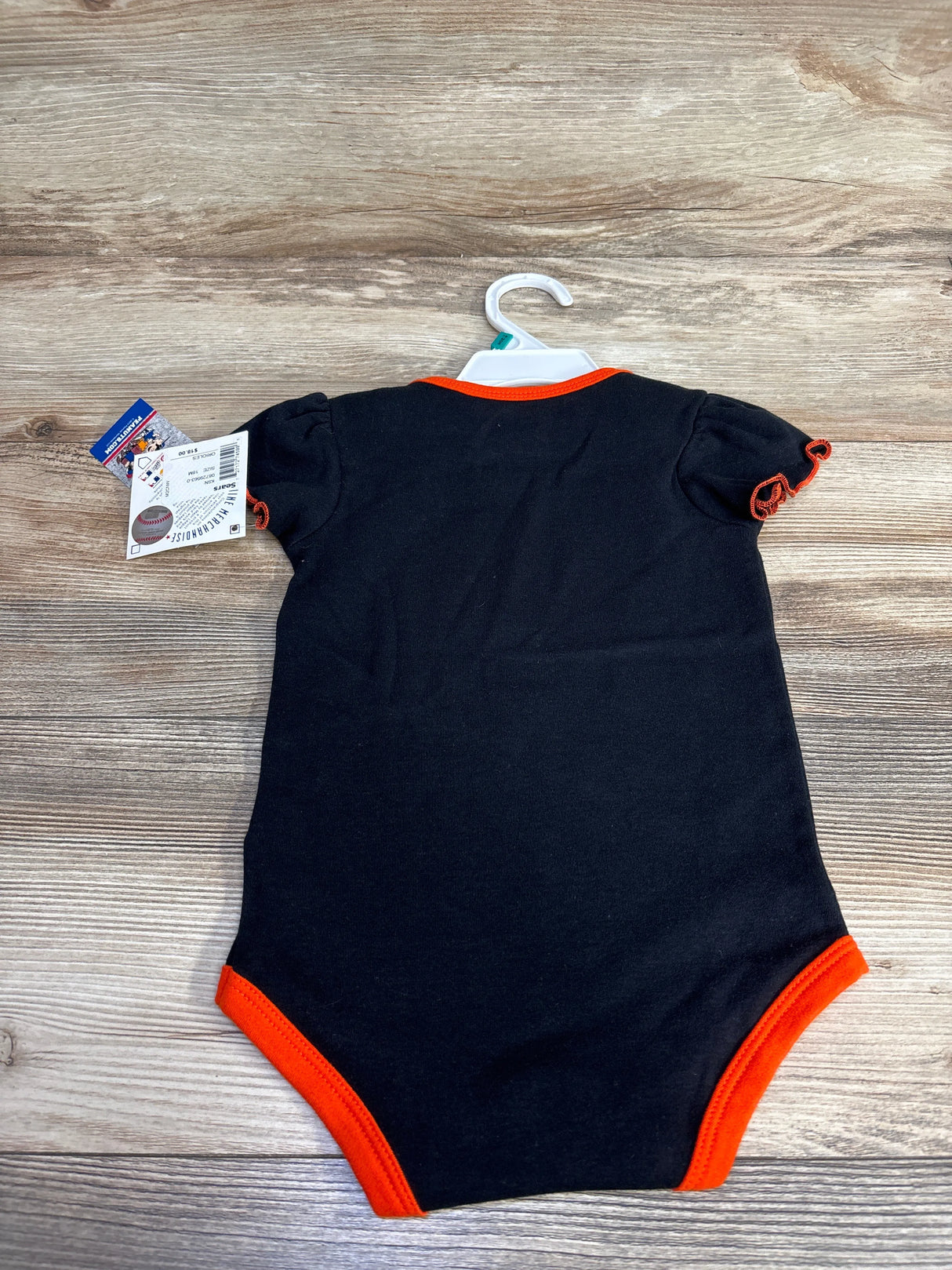 Black baby bodysuit with orange trim on hanger, displayed on wood surface