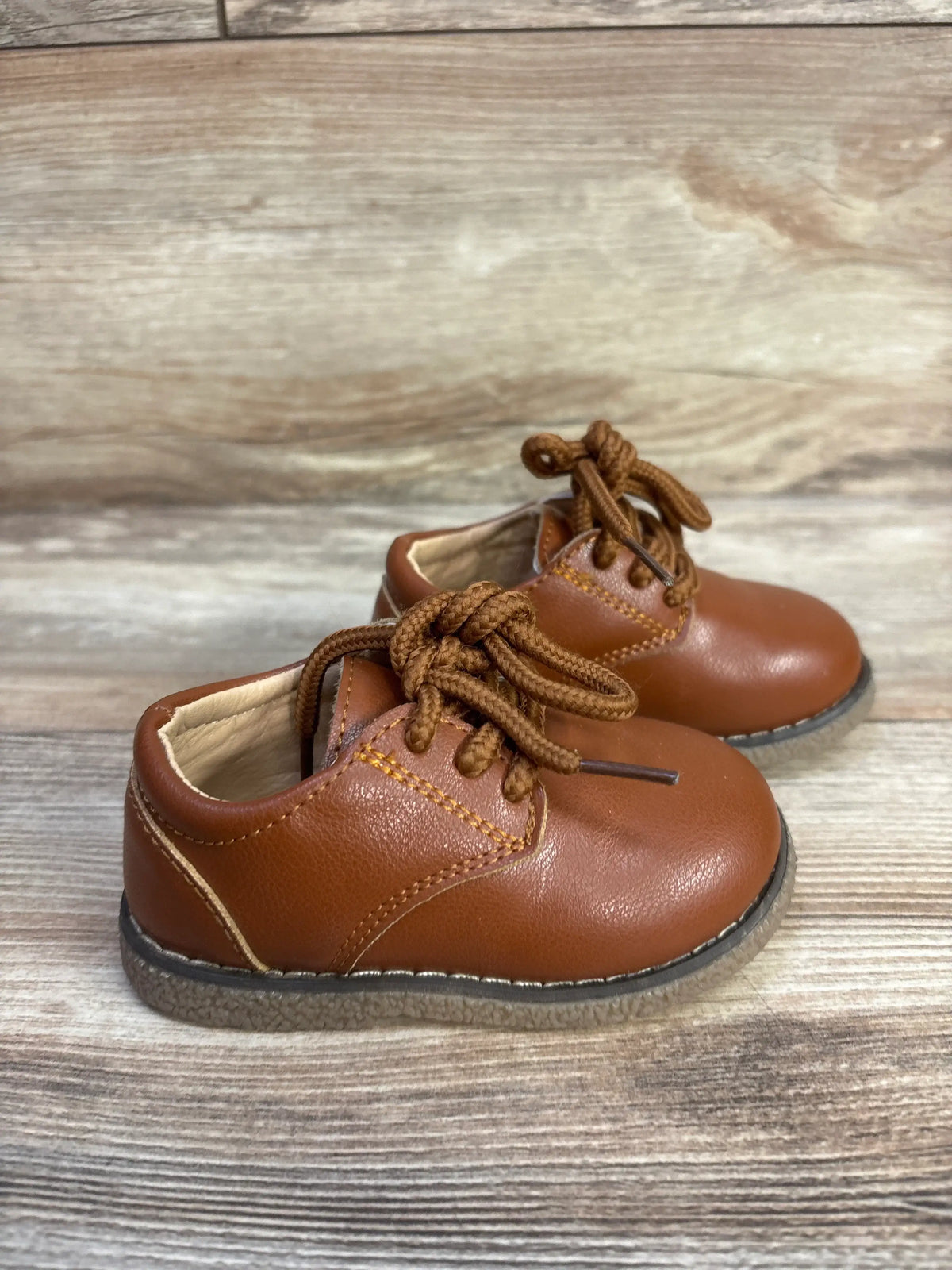 Front three-quarter view of Meckior Oxford Dress Shoes in brown showcasing lace-up closure and PU leather on a wood-grain surface
