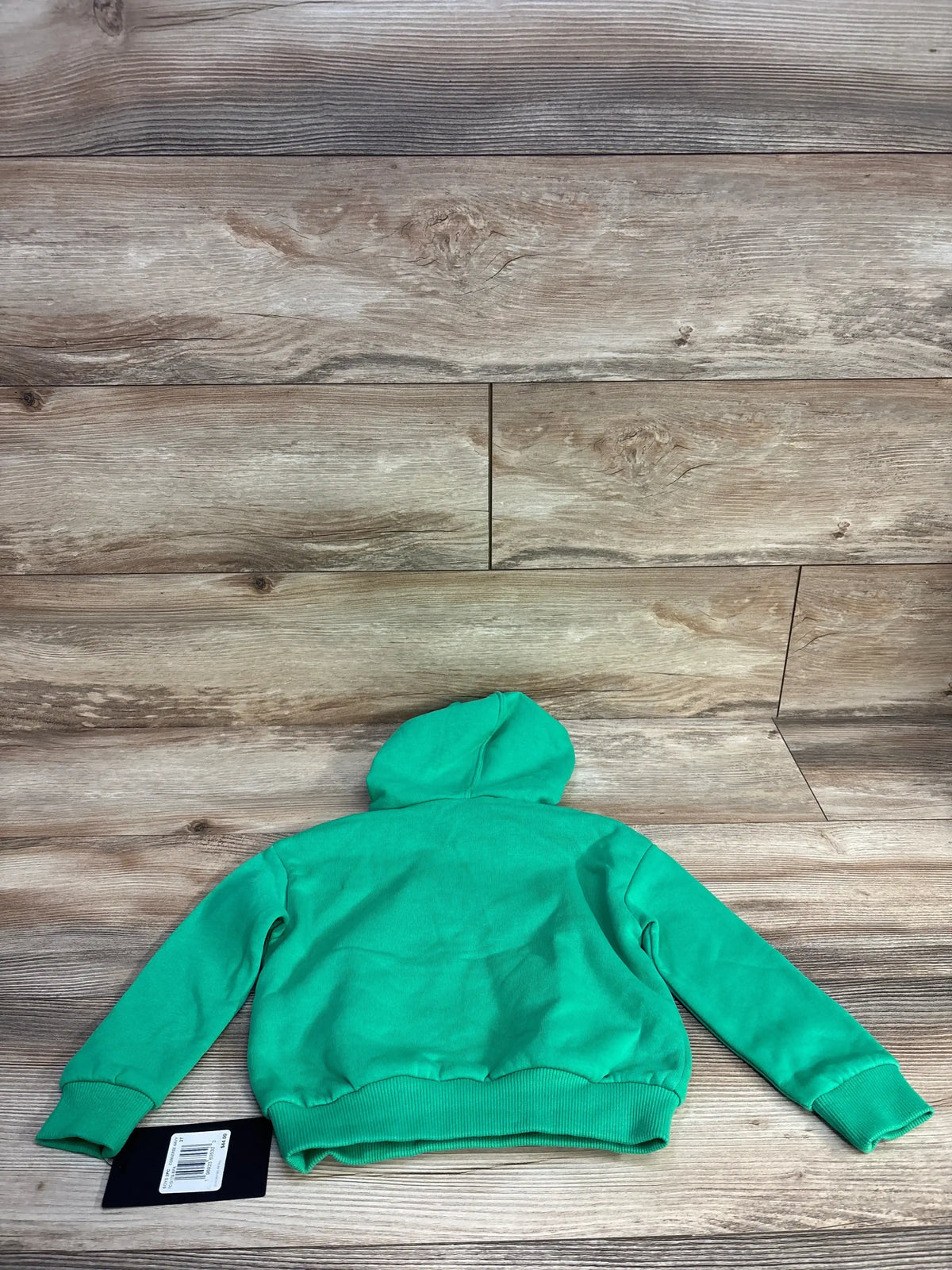 Green kids hoodie with tag displayed on wooden floor