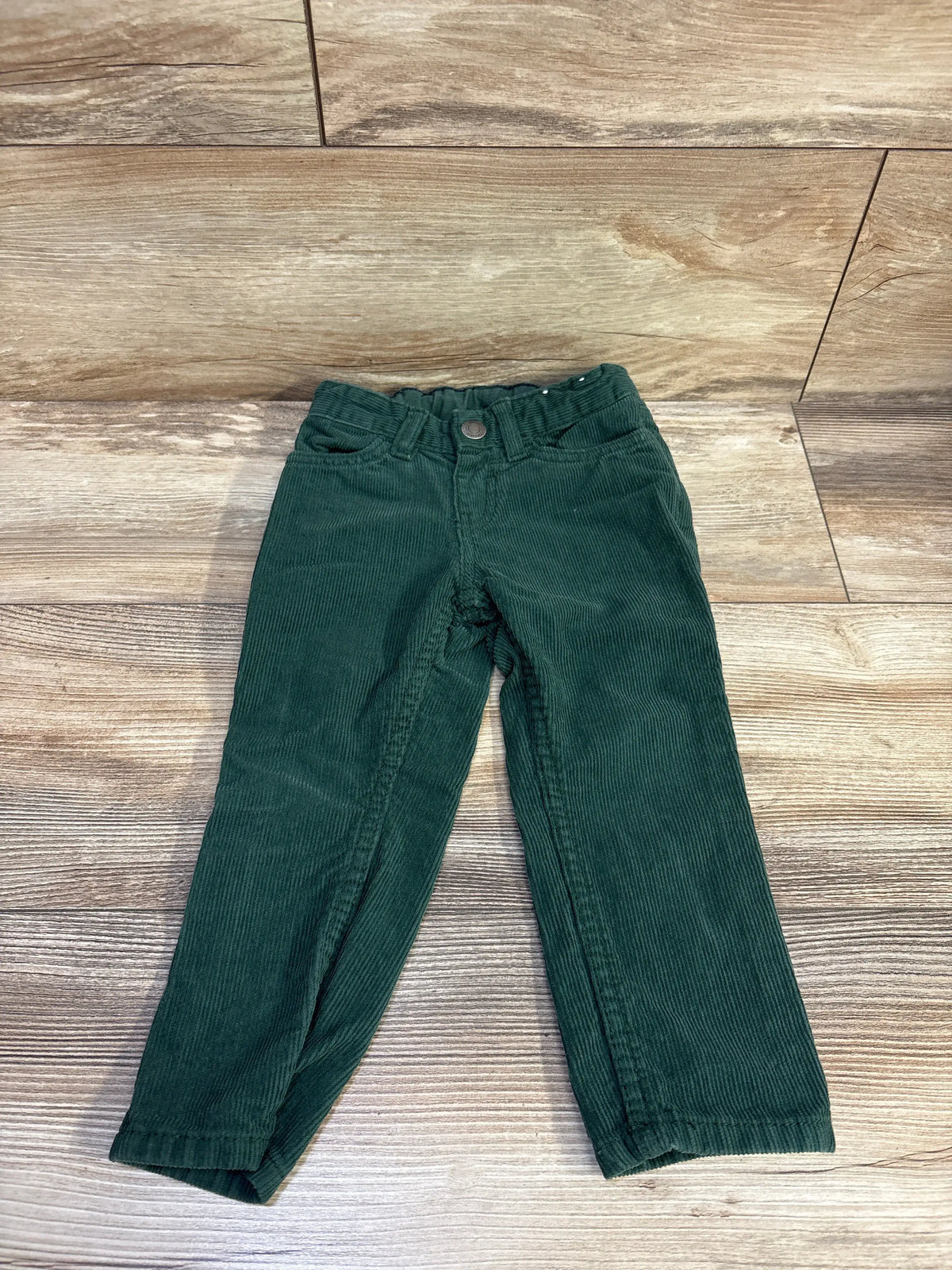 Front view of green H&M corduroy toddler pants size 2T showing slim fit, elastic-adjust waistband and front pockets on wood floor background