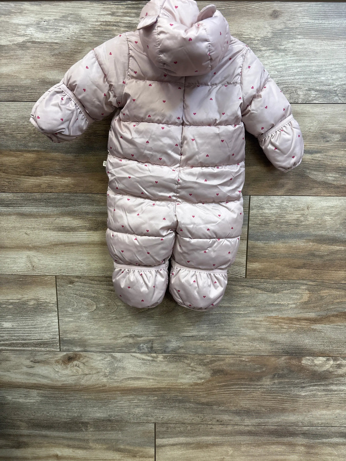 Flat lay of Baby Gap ColdControl Max snowsuit showcasing a pink heart pattern and hood on a wood floor