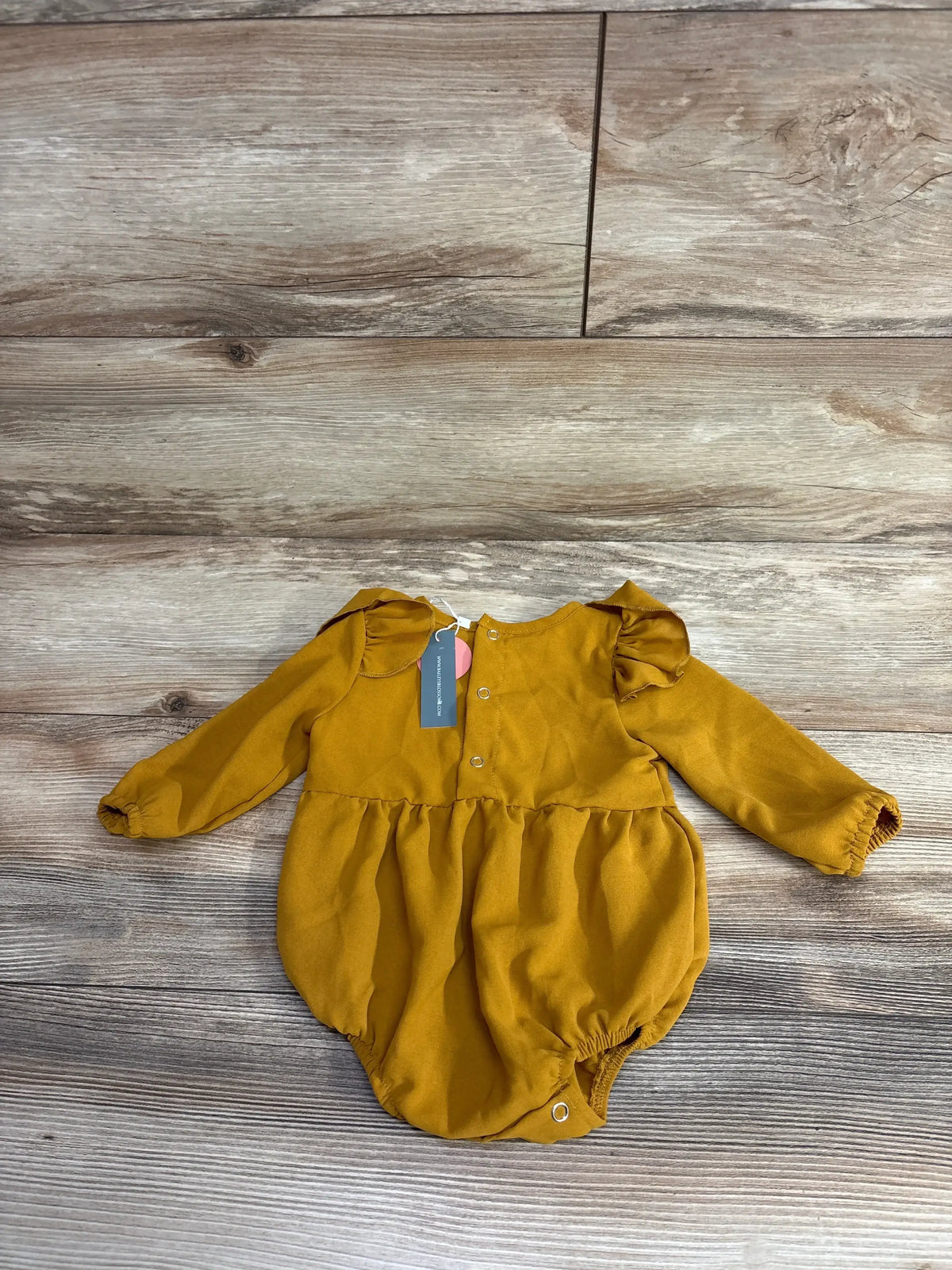 Mustard yellow long sleeve baby romper with ruffle shoulders on wood background