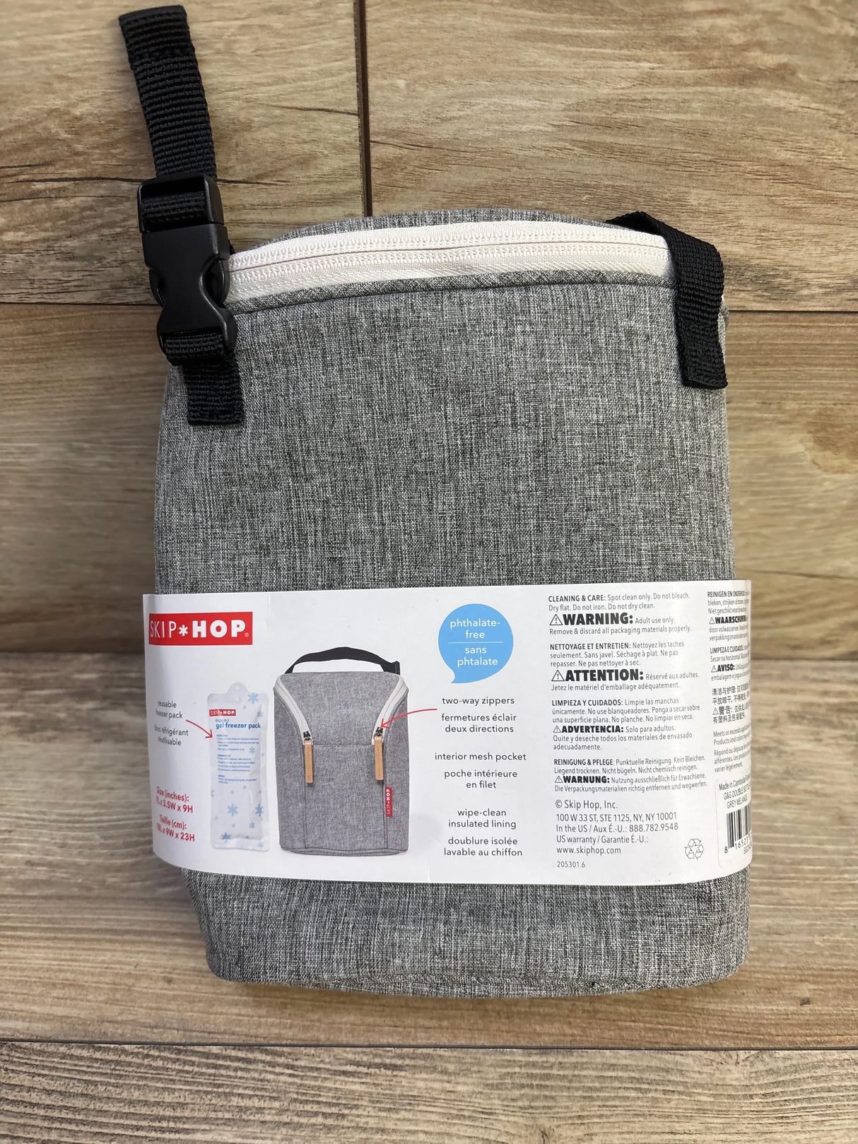 Front view of Skip Hop Grab & Go double bottle bag in grey showcasing white two-way zipper and top strap with buckle on wooden background