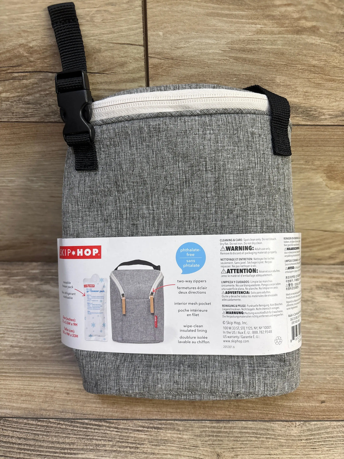 Front view of Skip Hop Grab & Go double bottle bag in grey showcasing white two-way zipper and top strap with buckle on wooden background