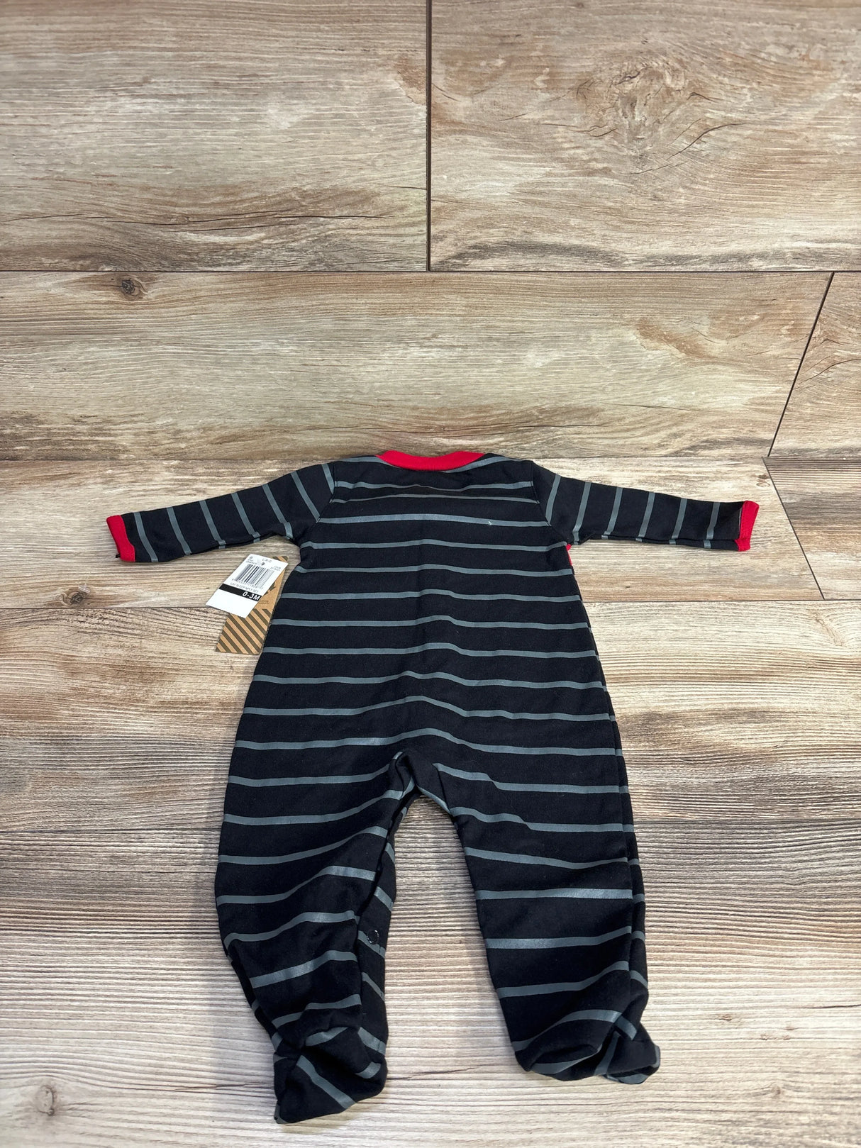 Striped black and gray long sleeve baby sleeper with red trim, laid flat on wood floor