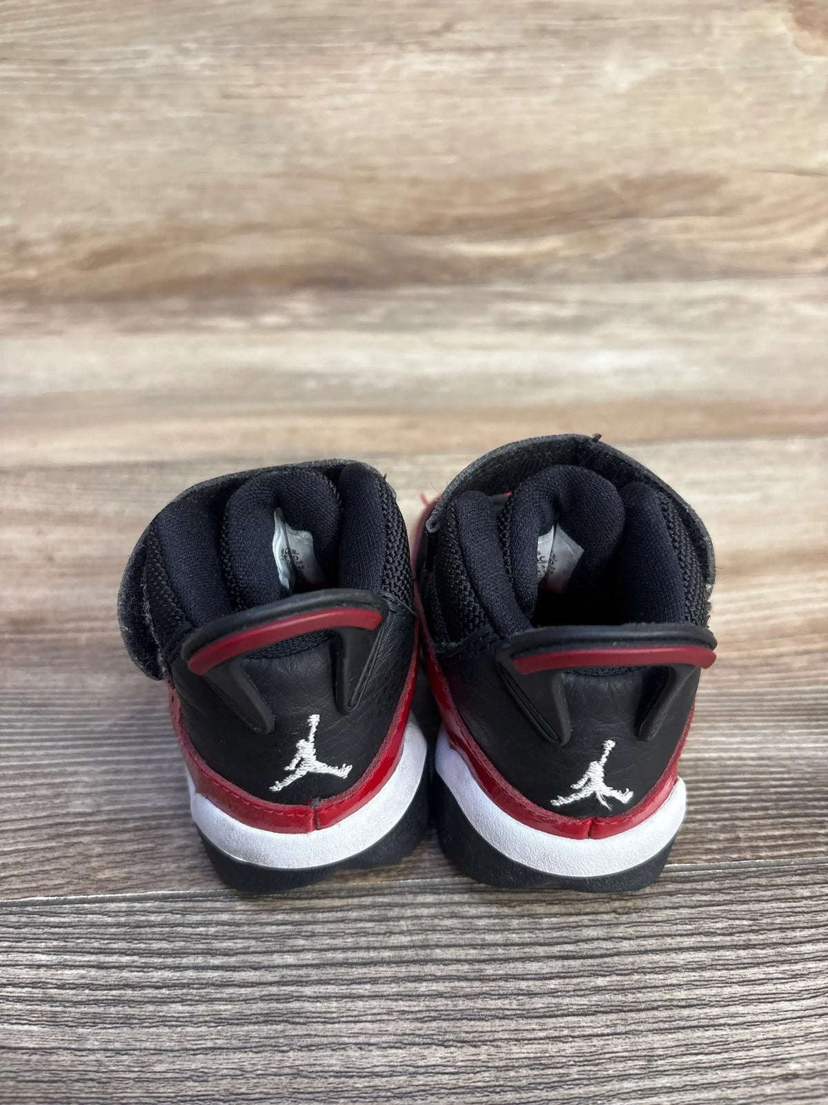 Rear view of toddler Jordan 6 Rings Fitness Red sneakers showing white Jumpman logo, black and red leather, on wood floor