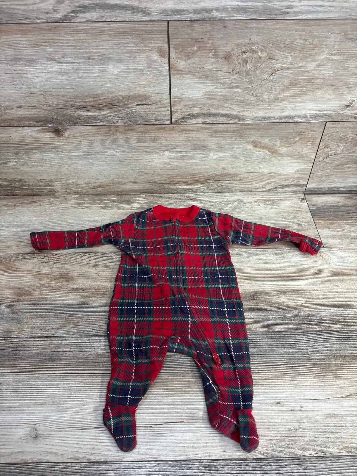 Red and green plaid baby footed pajamas with zipper, laid on wood floor