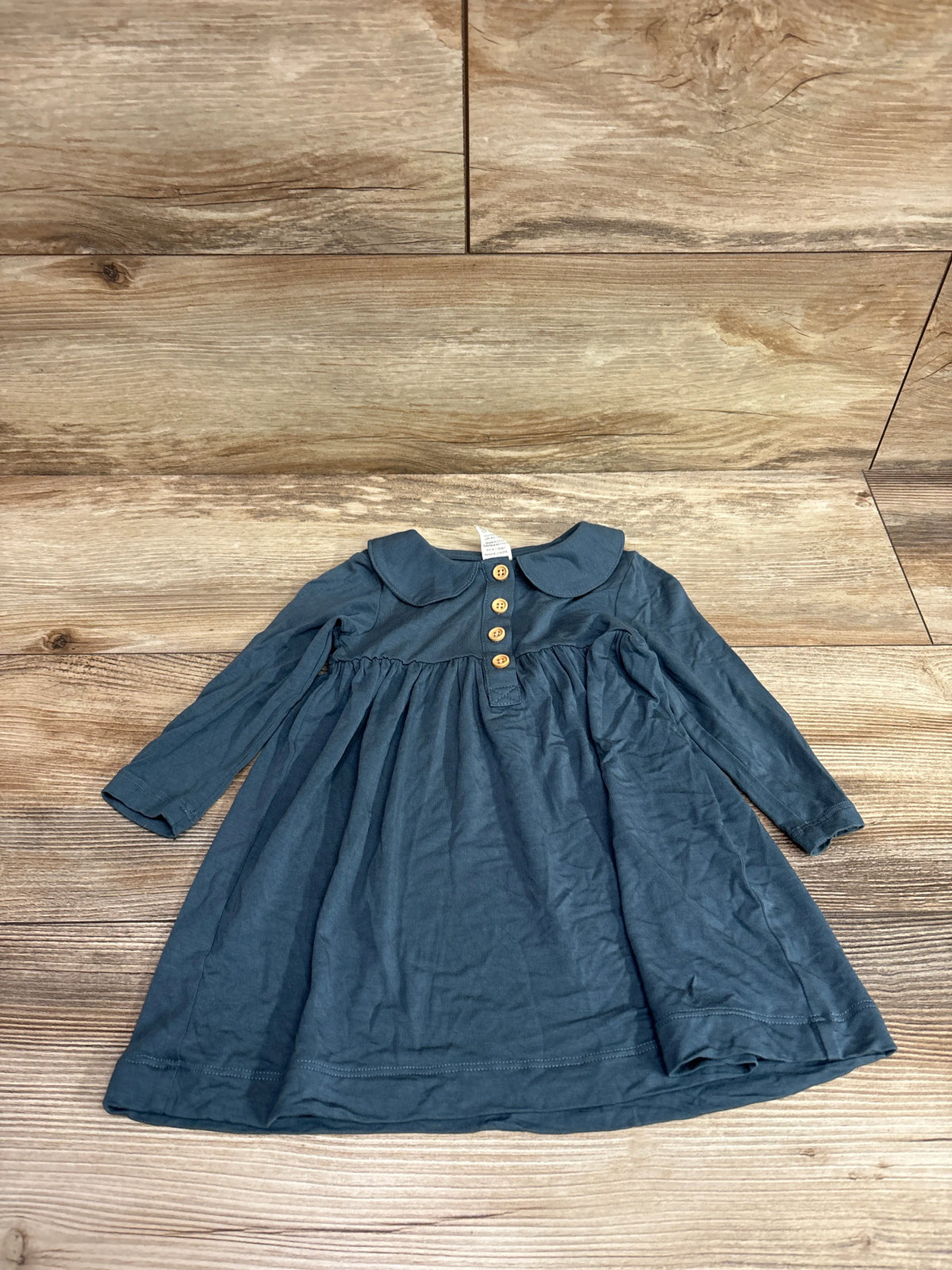 Front view of Kate Quinn blue Henley Peter Pan collar dress showing three-button placket and gathered skirt on wood