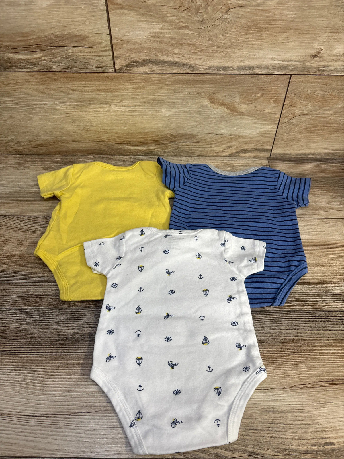 Top down view of Kiddiezoon three piece bodysuit set showing yellow, blue striped, and nautical print bodysuits on a wood floor