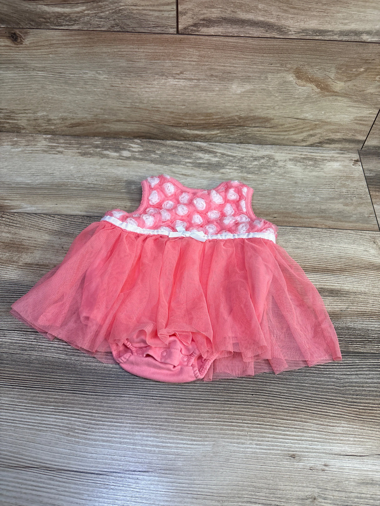 Flat-lay of Little Me bodysuit dress with coral tulle skirt, rosette bodice, ribbon trim and snap closures on wood