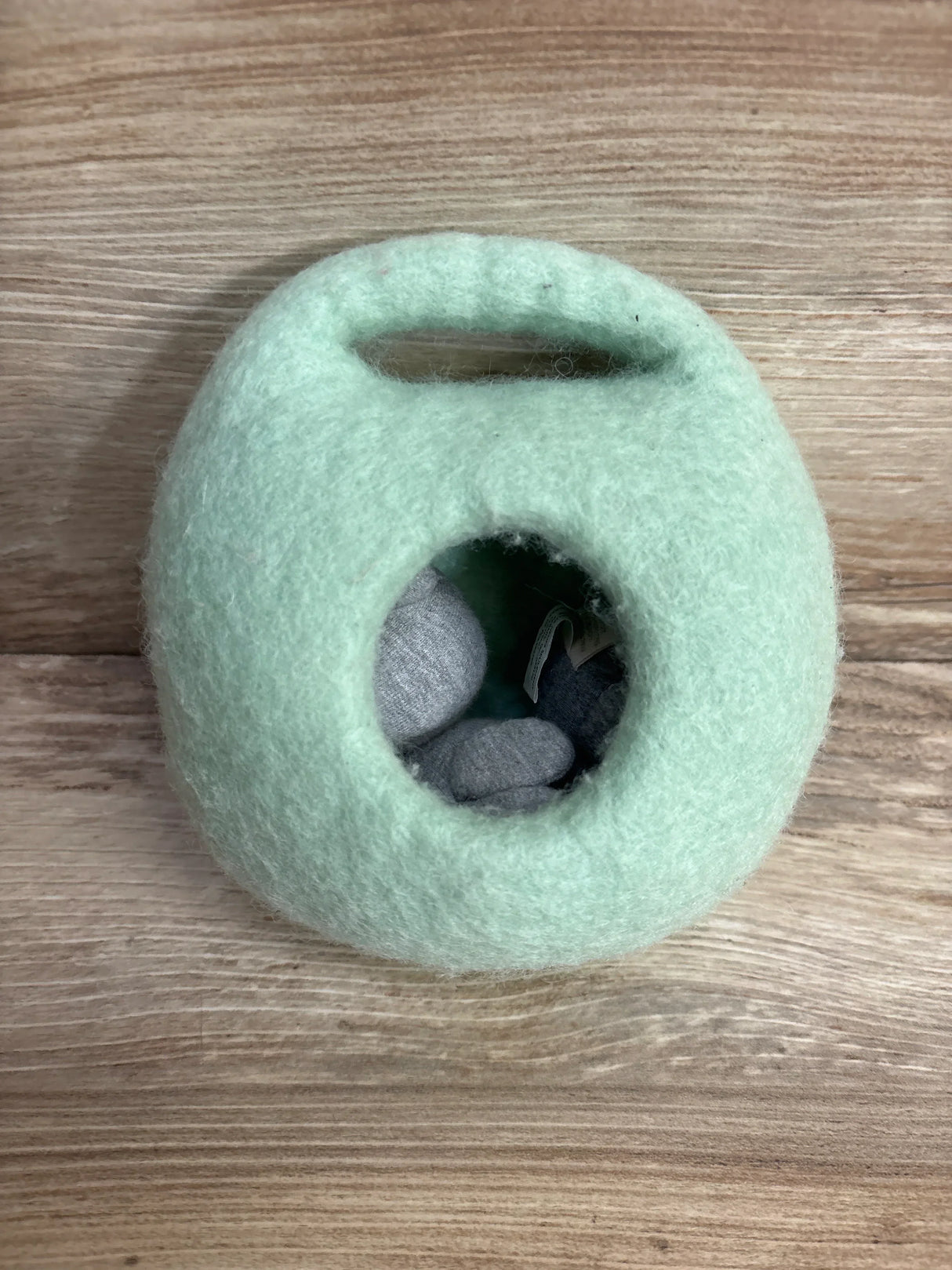 Mint green felted wool toy basket with grey soft toys on wood background