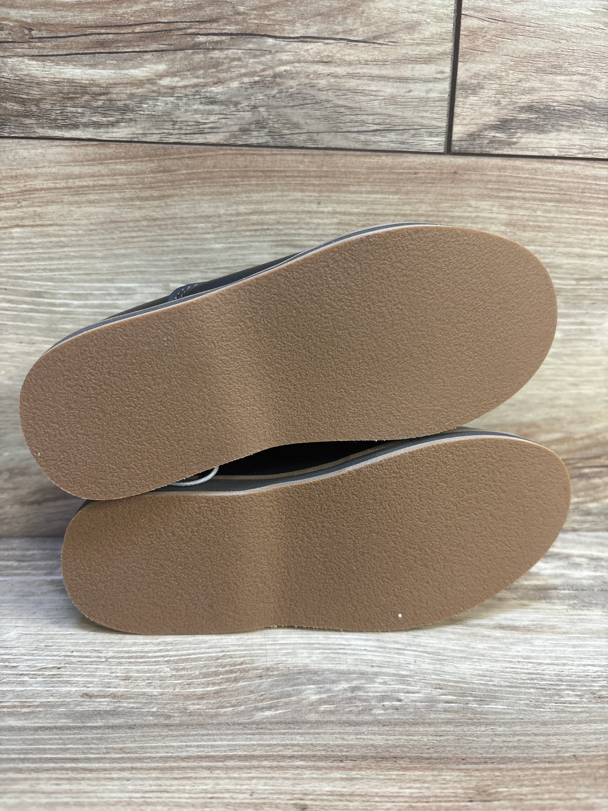 Pair of kids shoes with clean brown rubber soles on wood background