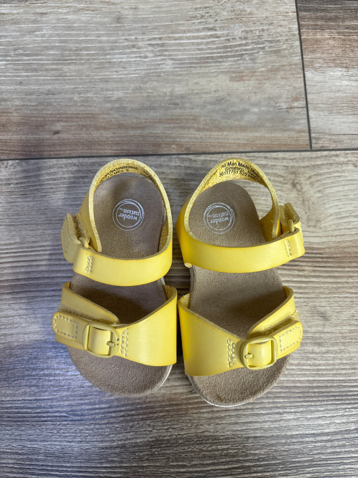 Top view of Wonder Nation yellow toddler buckle sandals showing two adjustable straps and cushioned footbed on wood floor