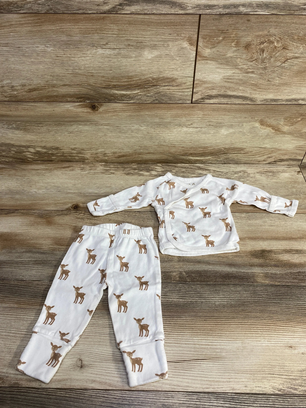 White baby pajamas set with brown deer print lying on wood floor, long sleeve top and pants