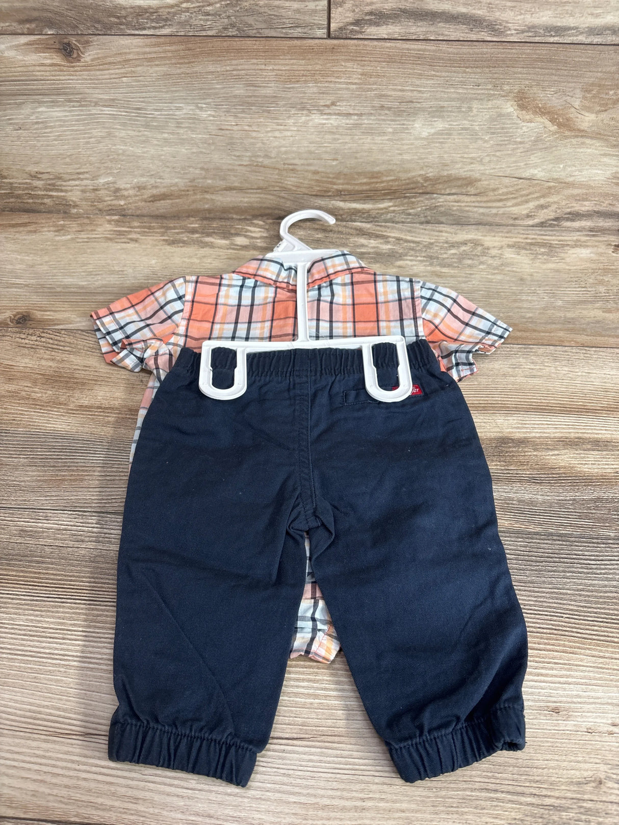Top-down view of Wrangler 2-piece orange plaid button-up bubble romper and navy pants on wood floor
