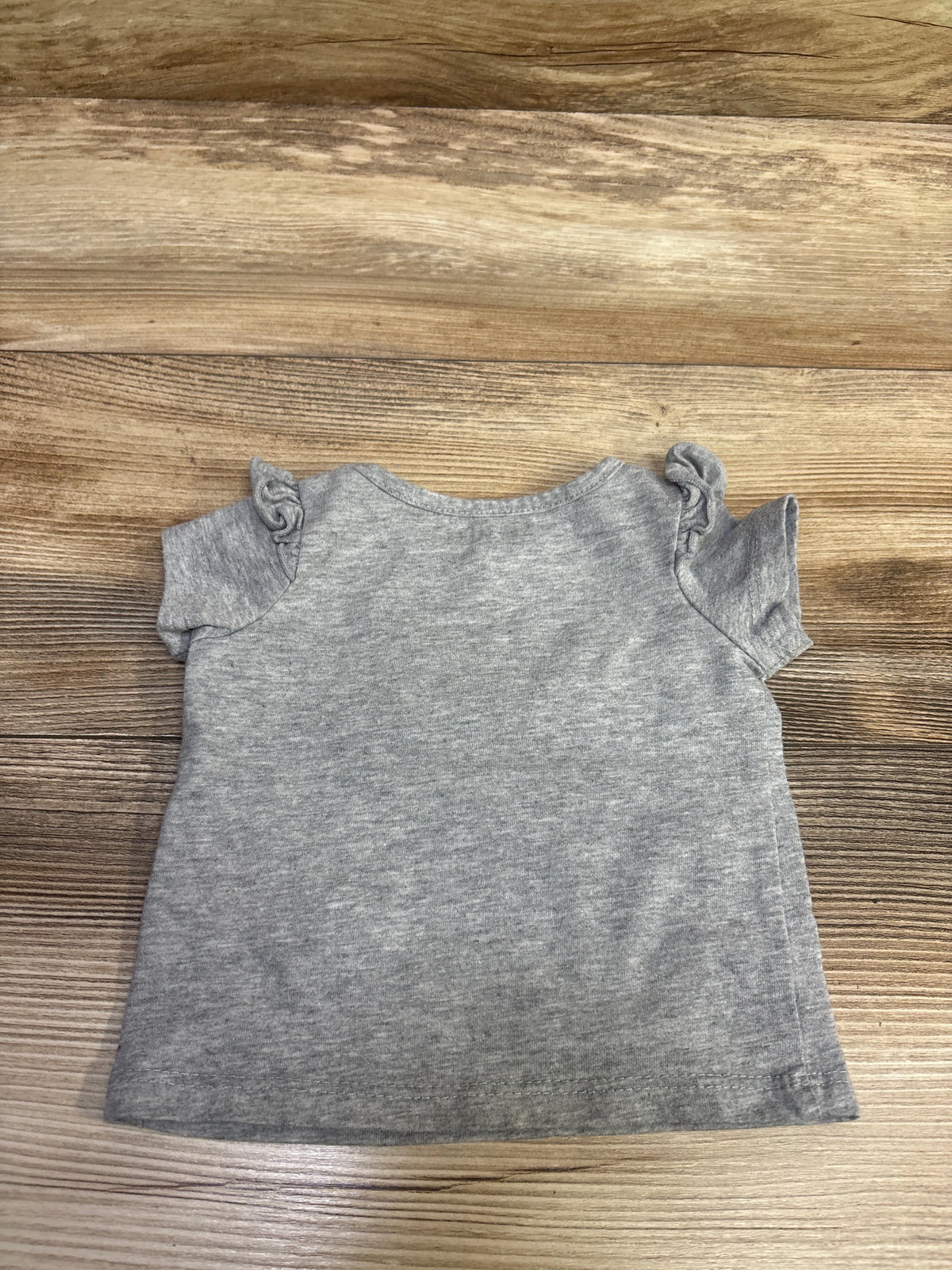 Top-down view of gray Okie Dokie All Good Vibes shirt in size 3 months showcasing ruffled sleeves on a wood background