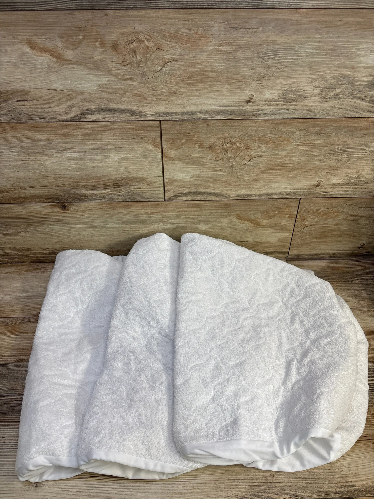 Folded angled view of 3-pack waterproof bassinet sheets showing textured waterproof surface and elastic edge on wood background