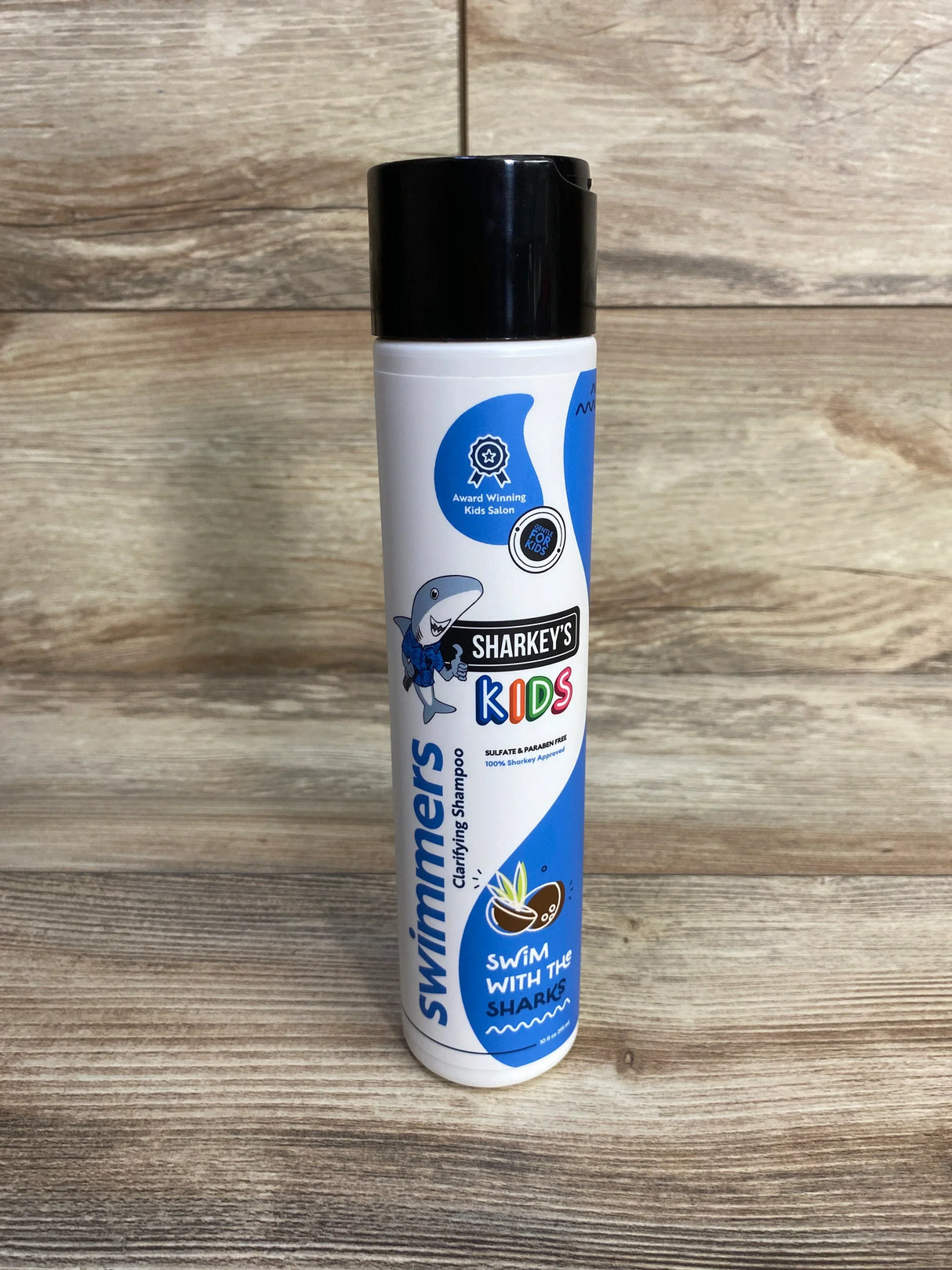 Front view of Sharkey's Swimmer's Clarifying Shampoo bottle showcasing Sharkey's Kids logo on a wood background