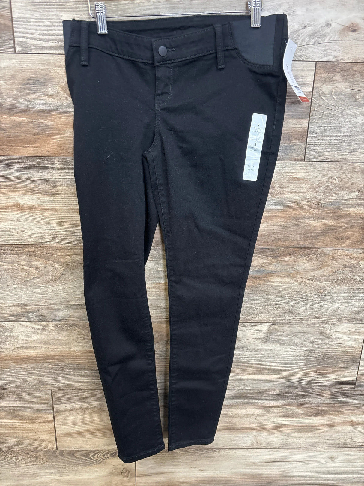 Front view of black Isabel maternity side-panel skinny jeans showing slim fit and elastic side panel on wood floor background