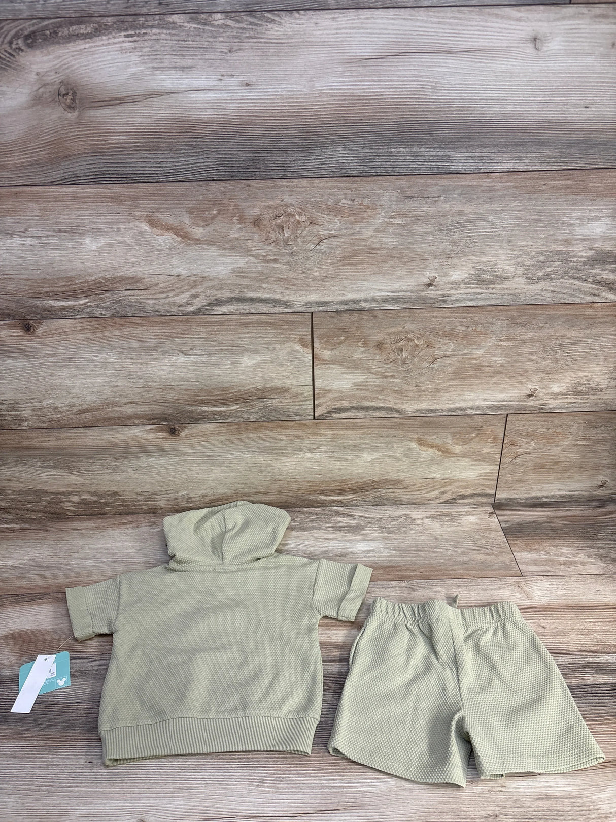 Flat lay of sage Disney Baby Winnie the Pooh 2-piece hooded shirt and shorts showing waffle knit texture and elastic waist on wood background
