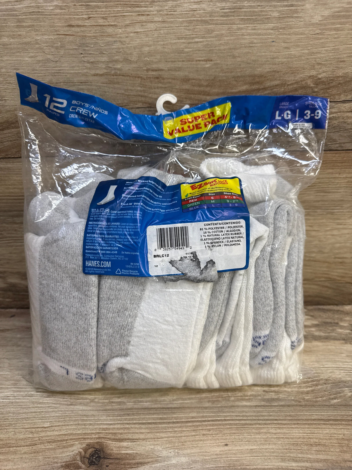 Front view of Hanes boys’ cushion crew socks 12-pack, size L (3-9Y), white and gray in clear packaging on wooden surface