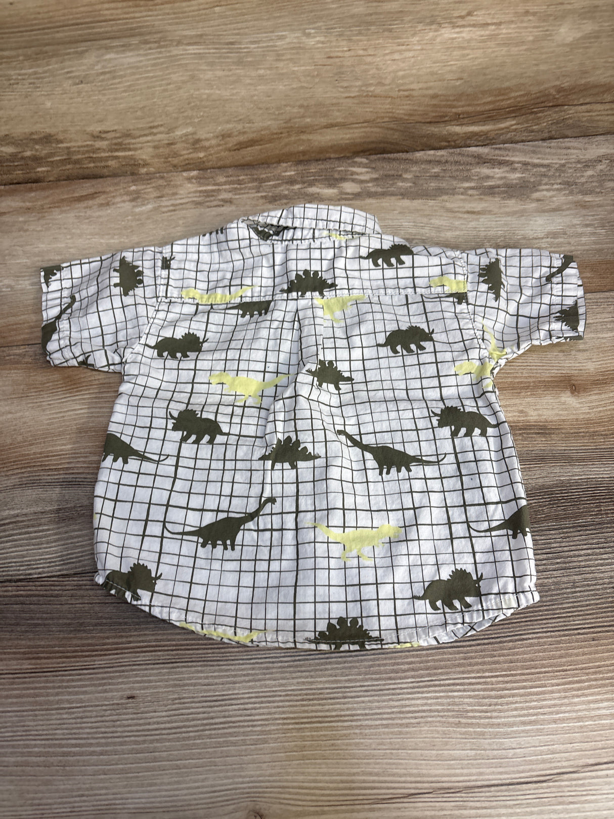 Kids' short sleeve dinosaur print button-up shirt on wooden background