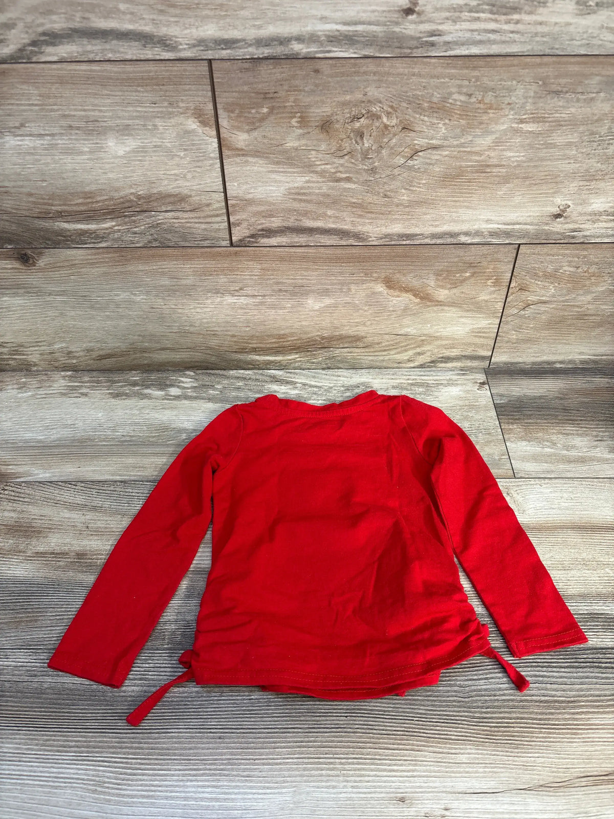 Back view of Disney Minnie Mouse heart shirt showcasing red long sleeves and side ties on a wood floor