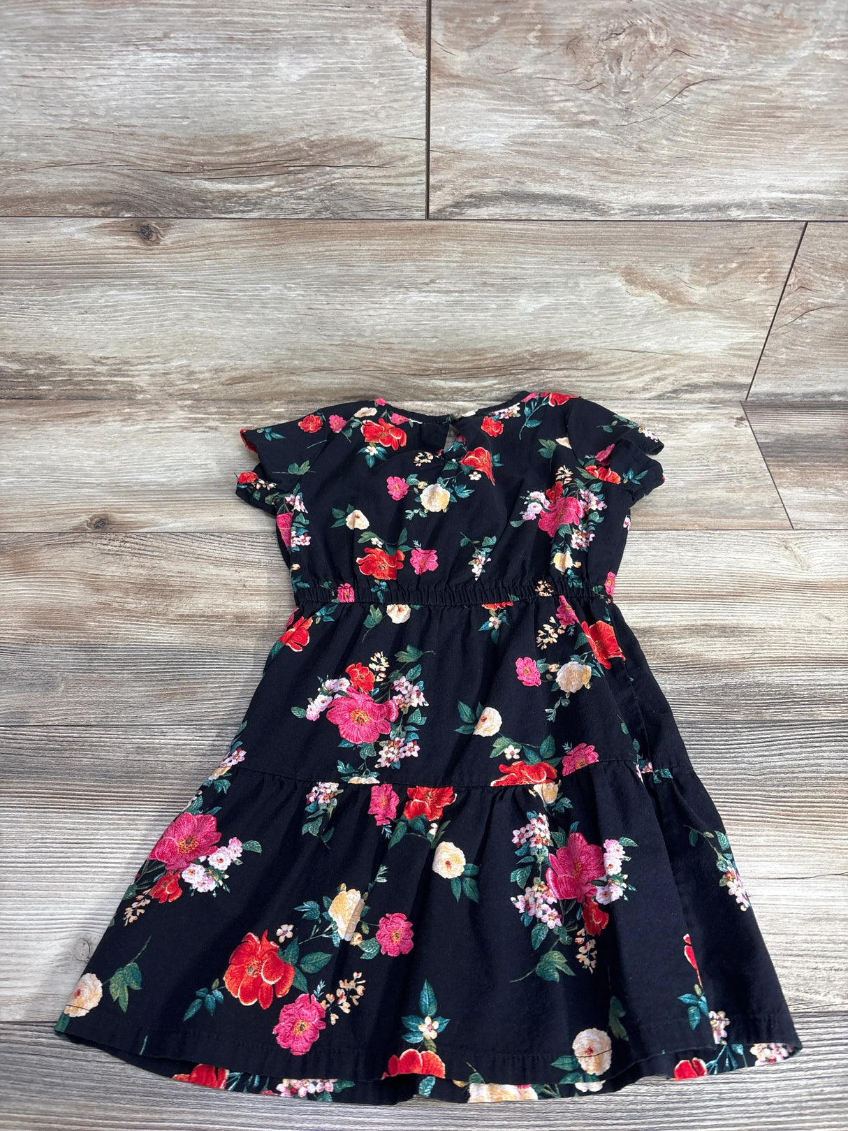 Black floral girls dress with short sleeves and colorful flower print on wood background