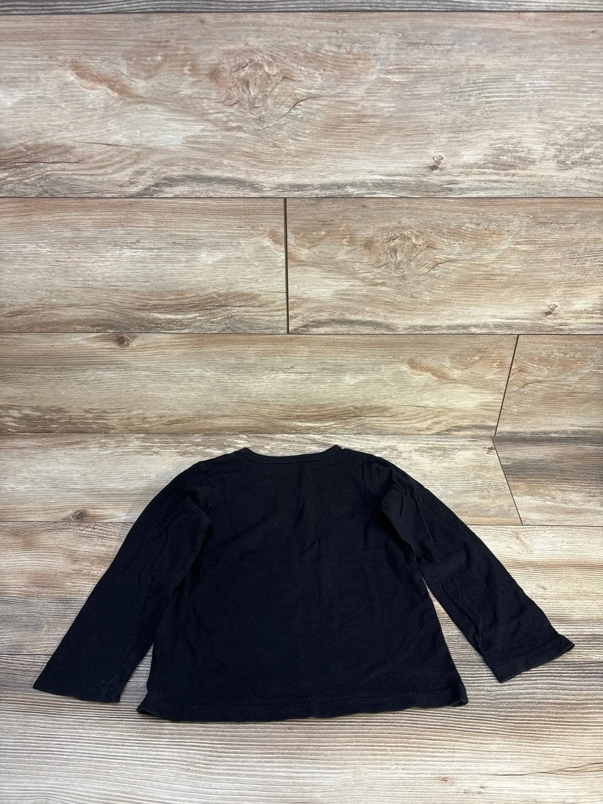 Black long sleeve kids shirt laid flat on wooden floor