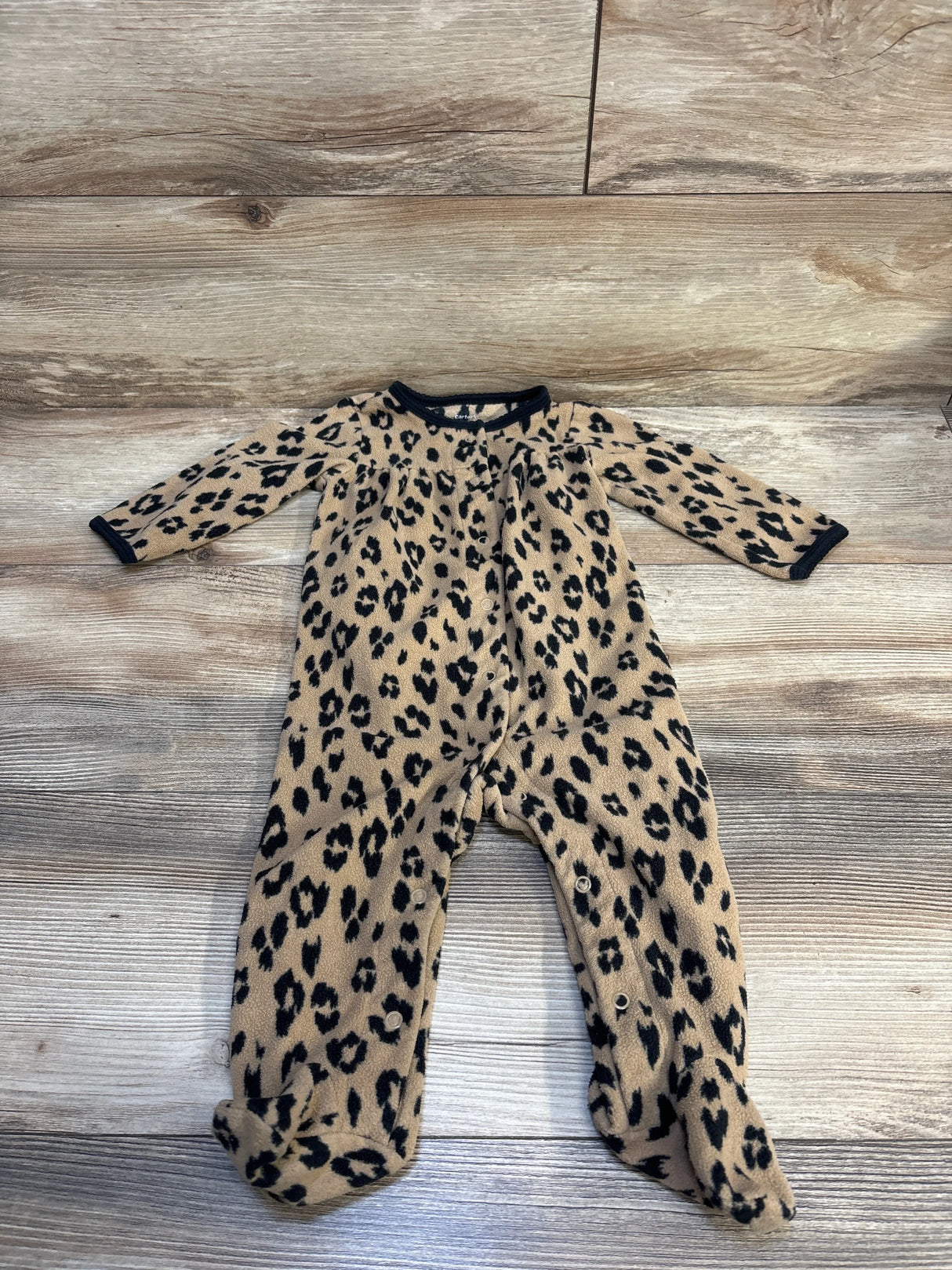 Leopard print baby sleeper with black trim, long sleeves, and footed design on wood floor