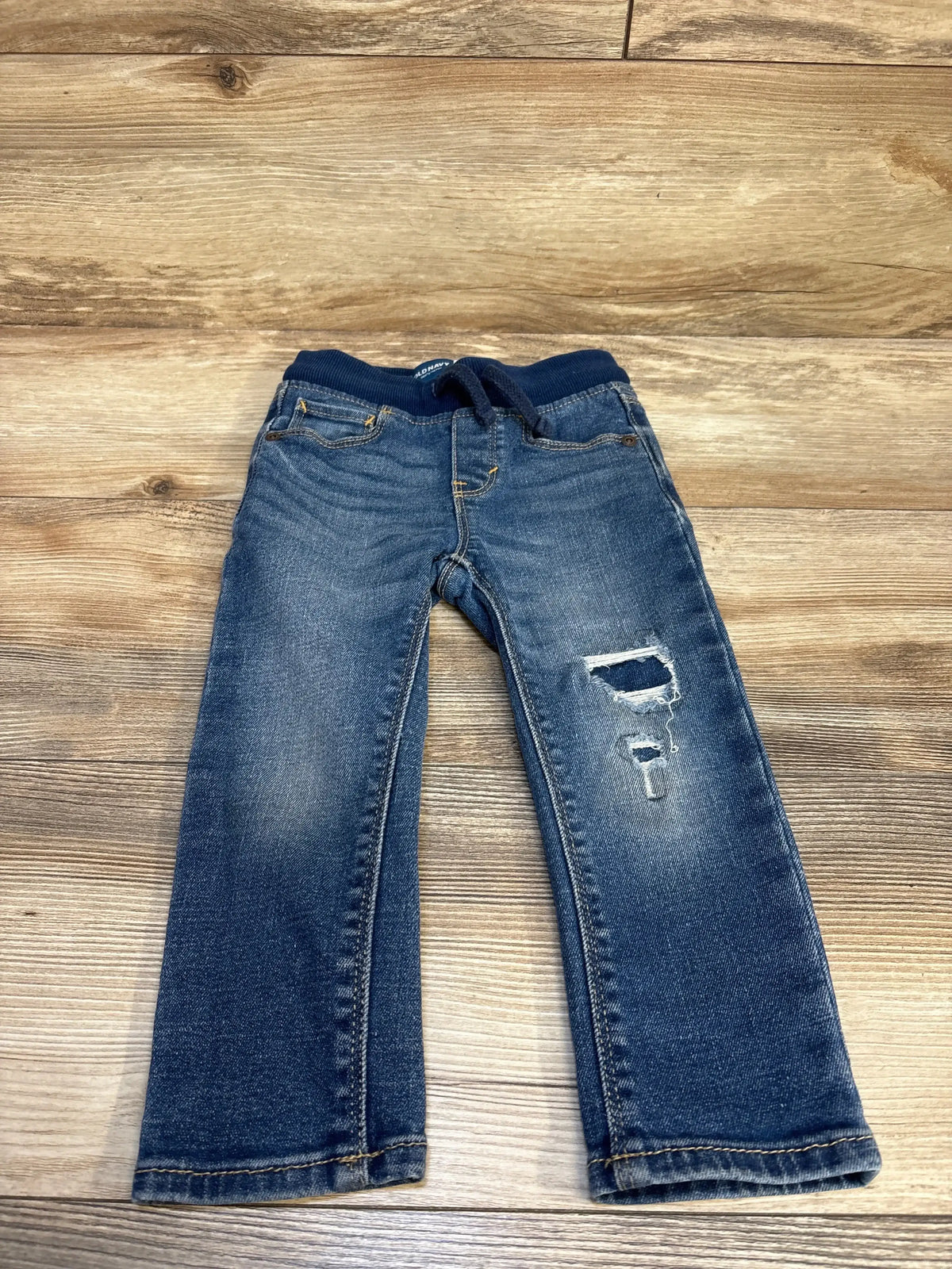 Kids' distressed denim jeans with ripped knee, laid on wooden floor